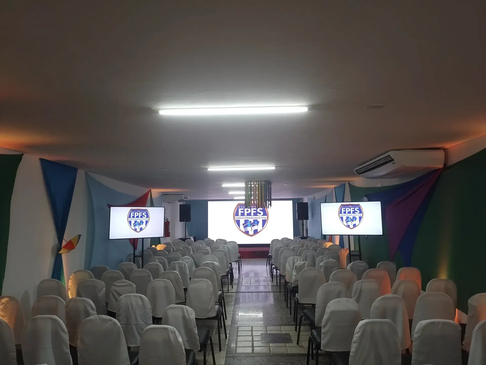Uma longa fileira de cadeiras em uma sala com uma tela grande no teto.