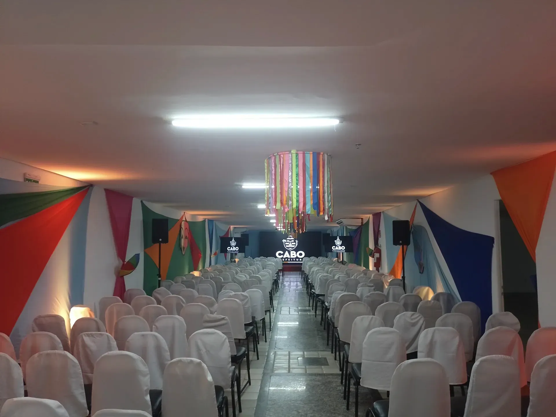 Um longo corredor com fileiras de cadeiras e um lustre pendurado no teto.