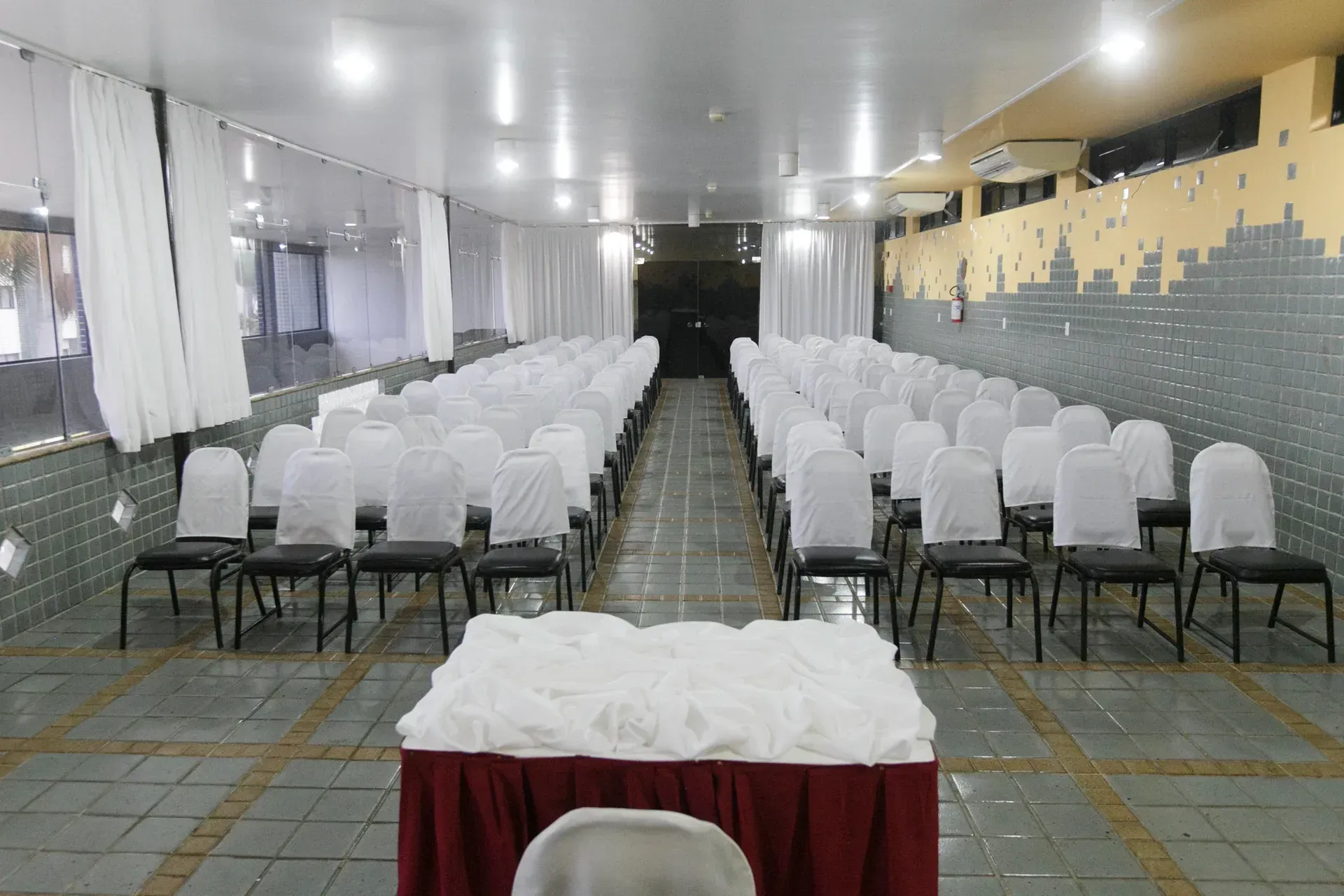 Uma sala longa com fileiras de cadeiras e uma mesa no meio.