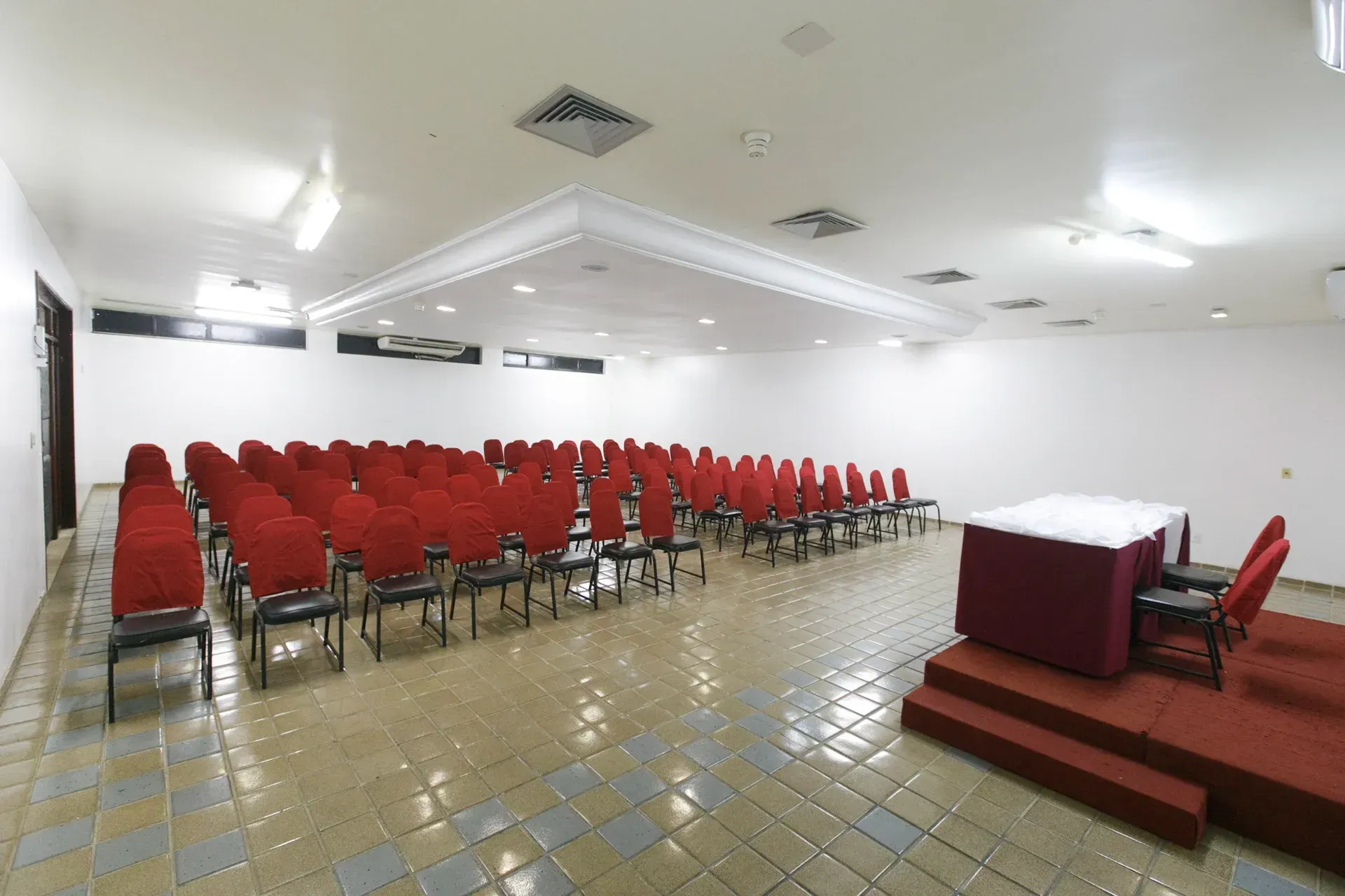 Uma sala grande com fileiras de cadeiras vermelhas e uma mesa