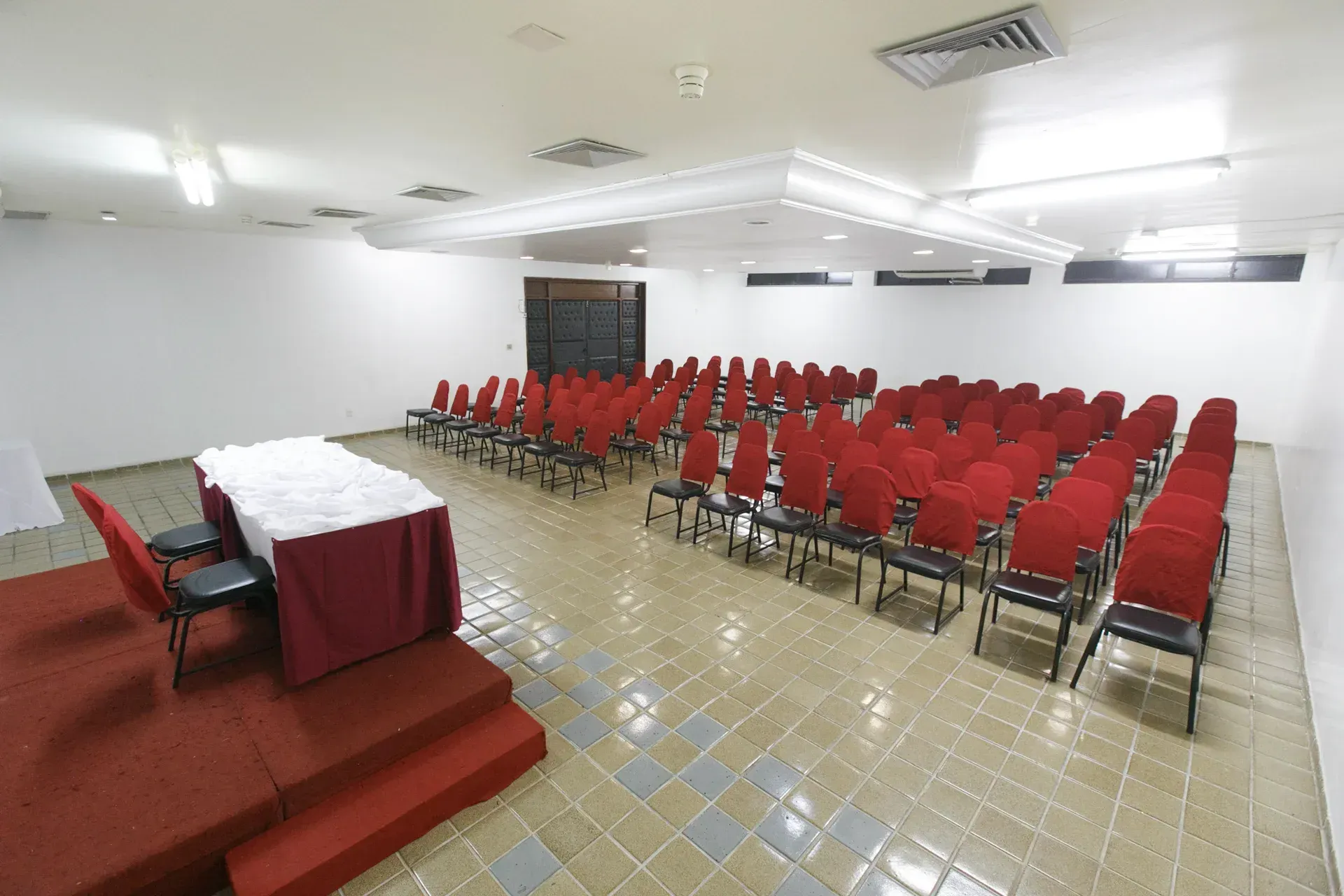 Uma sala grande com fileiras de cadeiras vermelhas e uma mesa