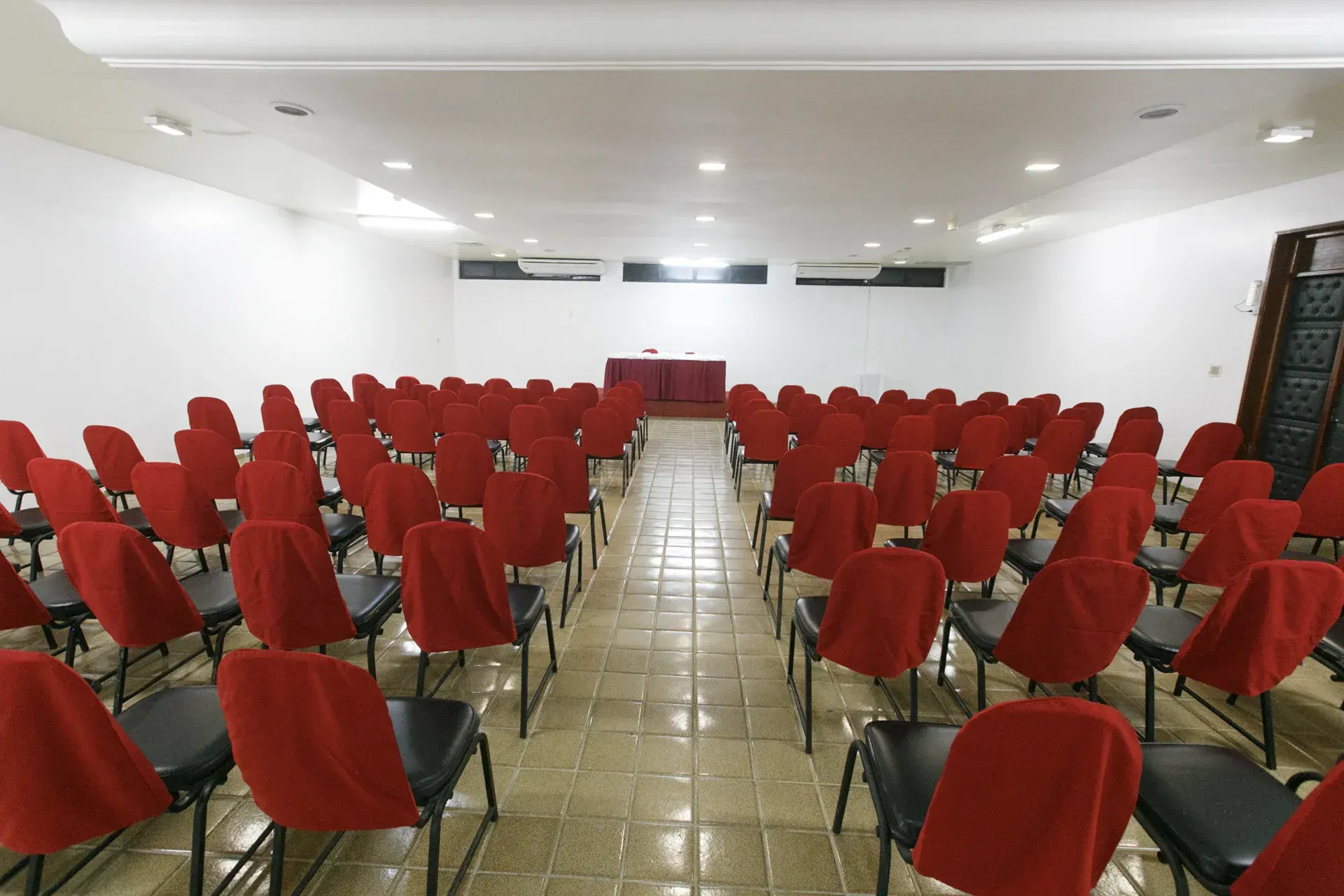 Fileiras de cadeiras vermelhas estão alinhadas em uma grande sala.
