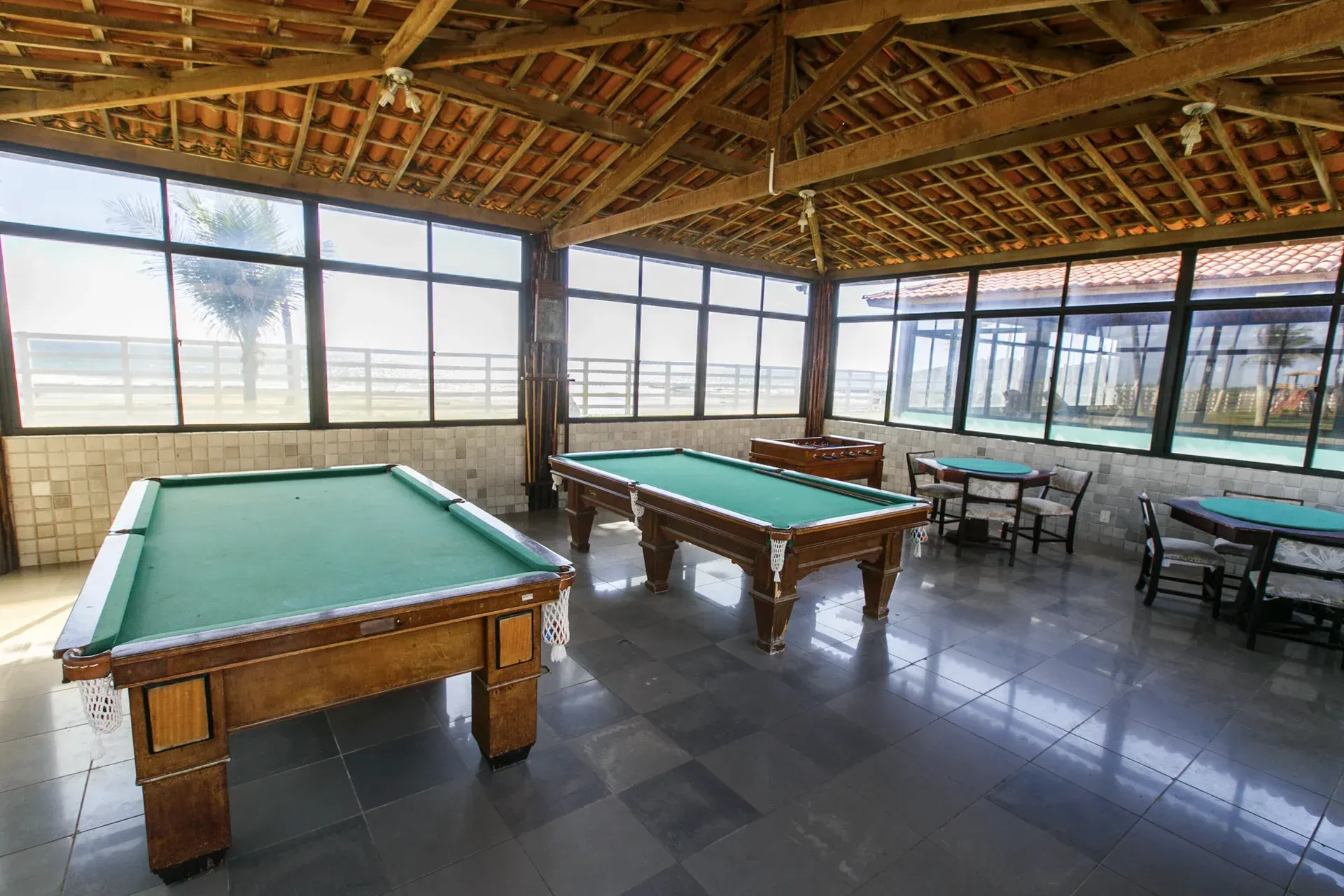 Duas mesas de sinuca estão em uma sala com muitas janelas.