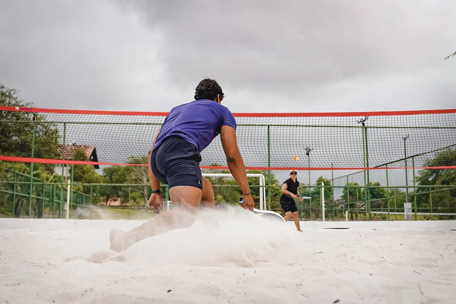 Duas pessoas estão jogando vôlei em uma quadra de areia.