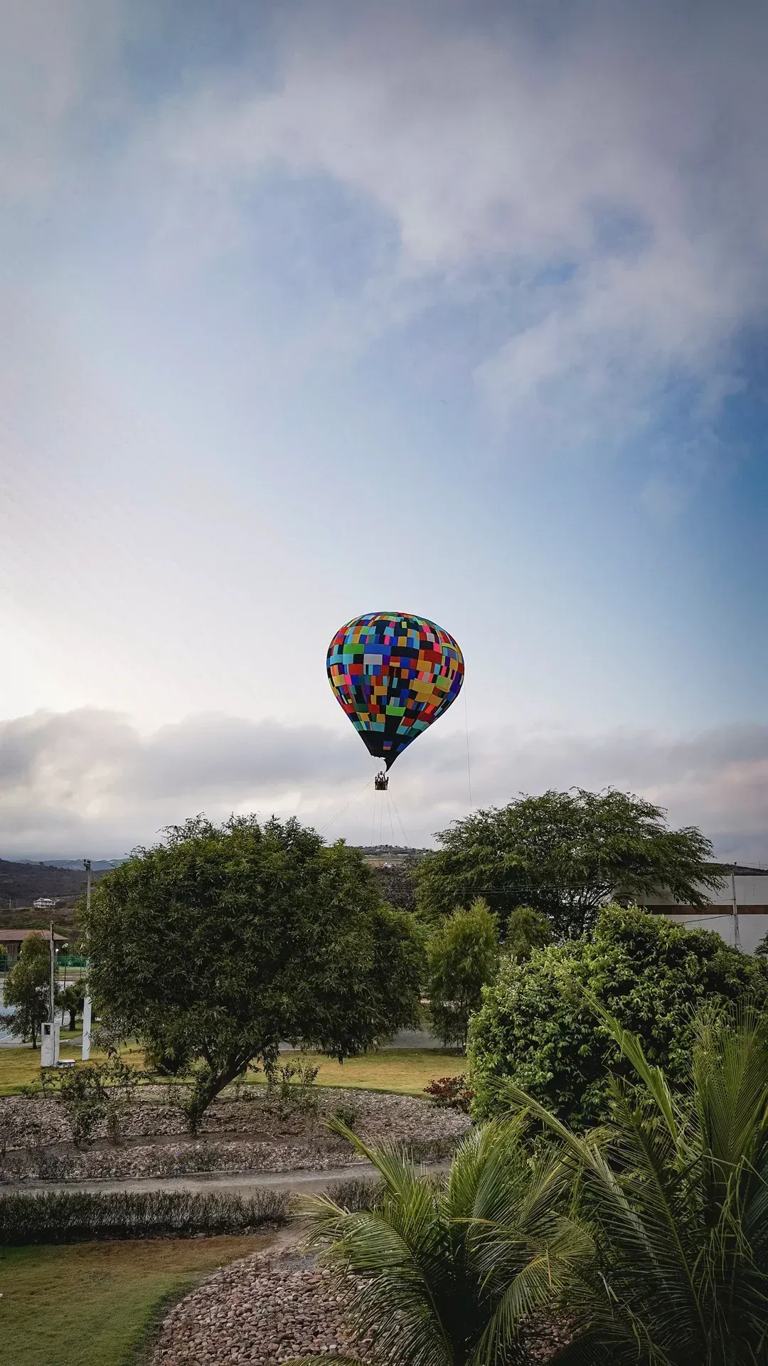 Um balão de ar quente colorido está voando no céu sobre um parque.