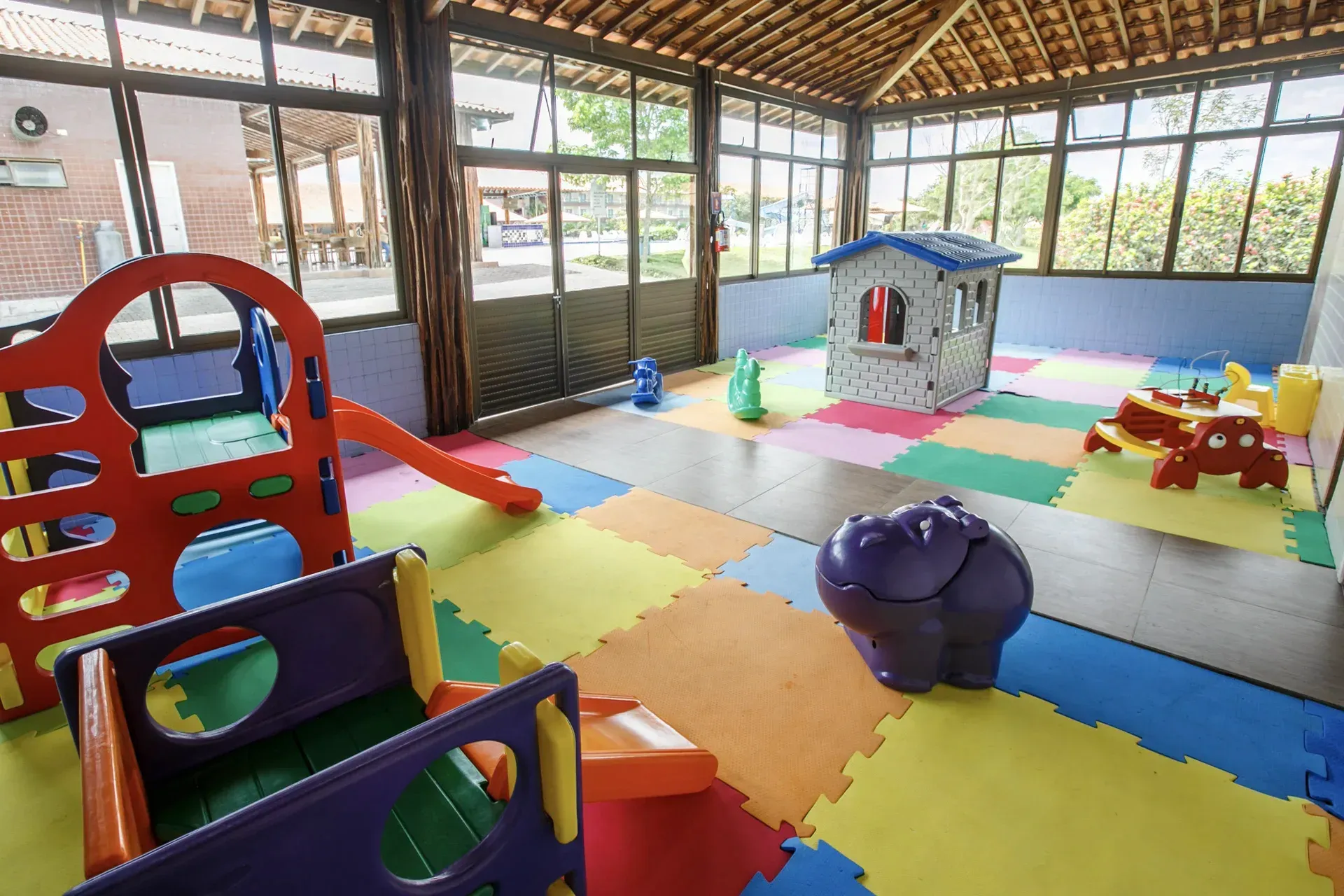 Um playground colorido com escorregador, balanços e uma casa.