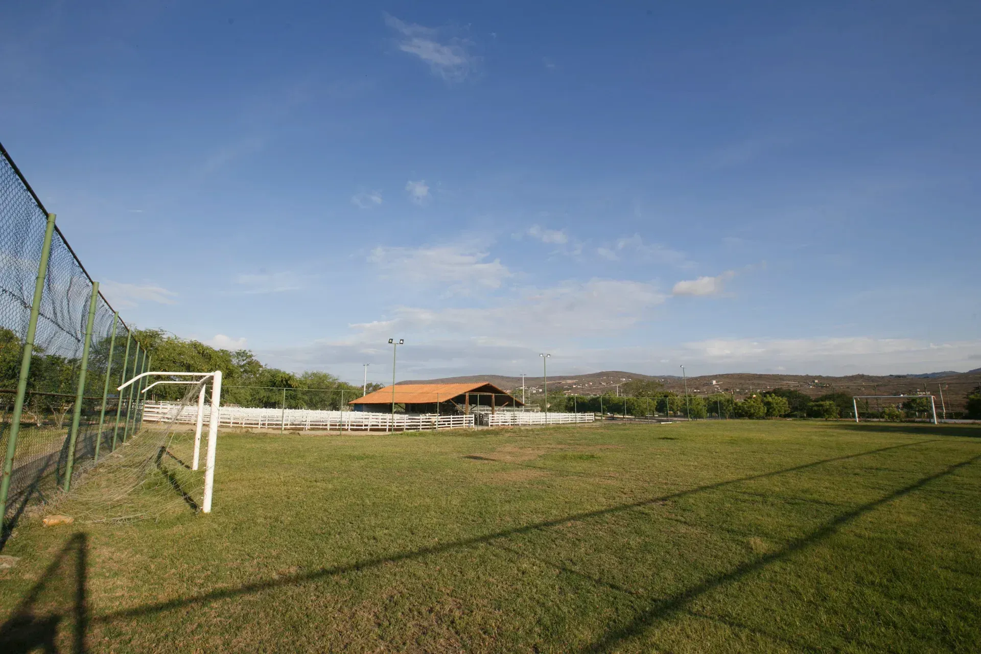 Um campo de futebol com uma cerca e um prédio ao fundo.