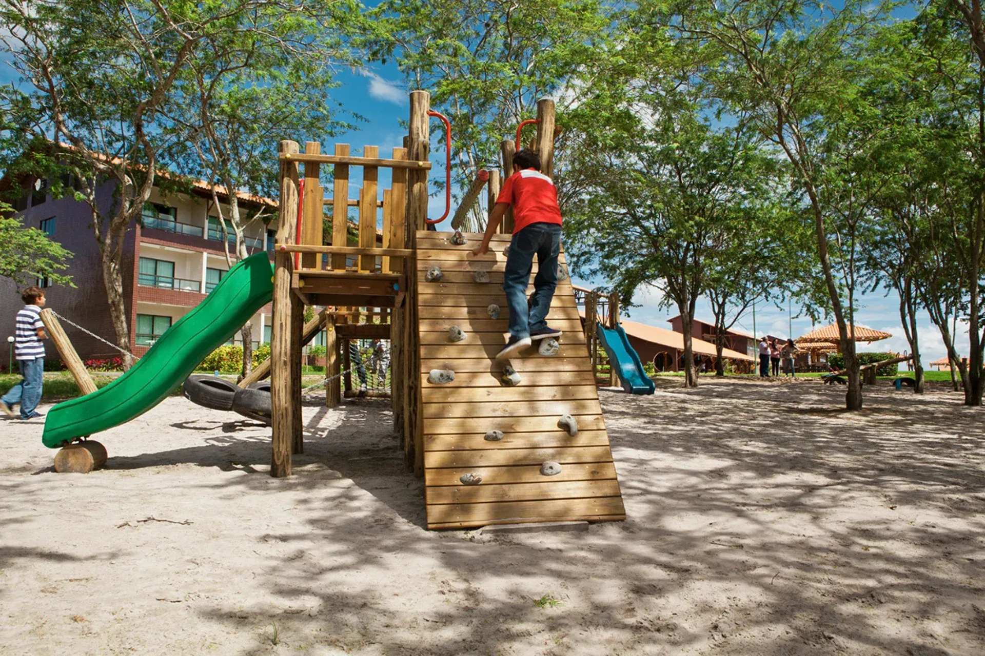 Uma criança está brincando em um playground de madeira com um escorregador verde.