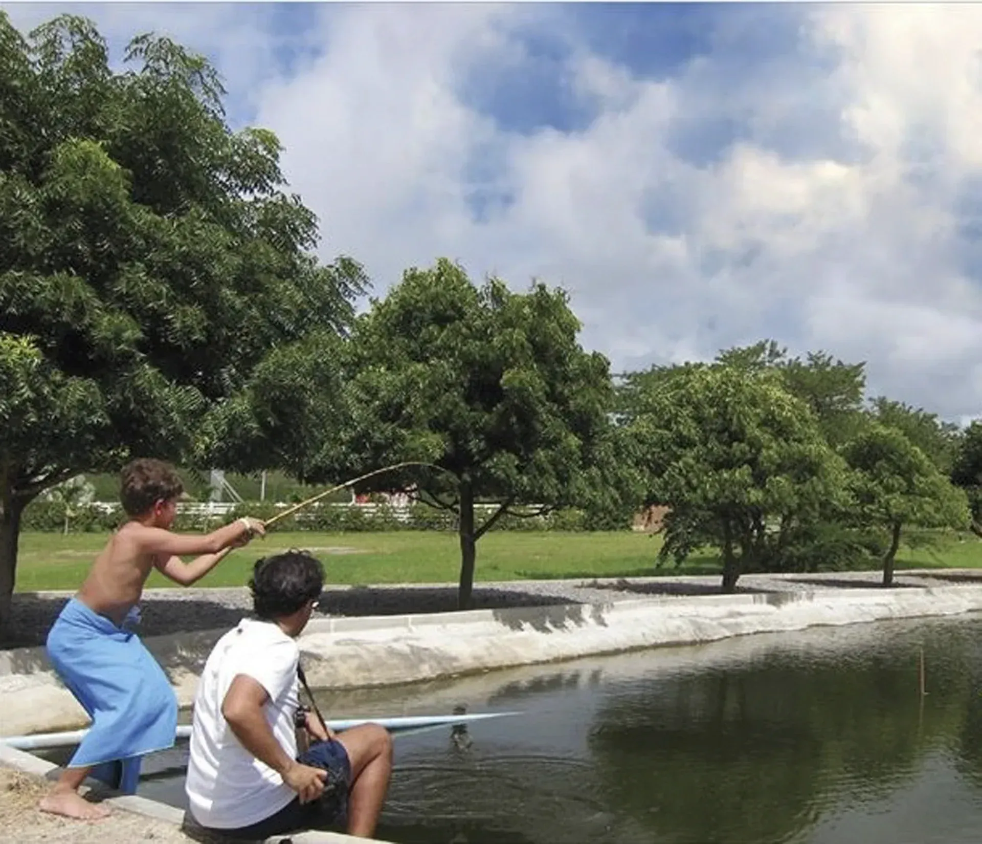 Dois meninos estão pescando em um lago com árvores ao fundo
