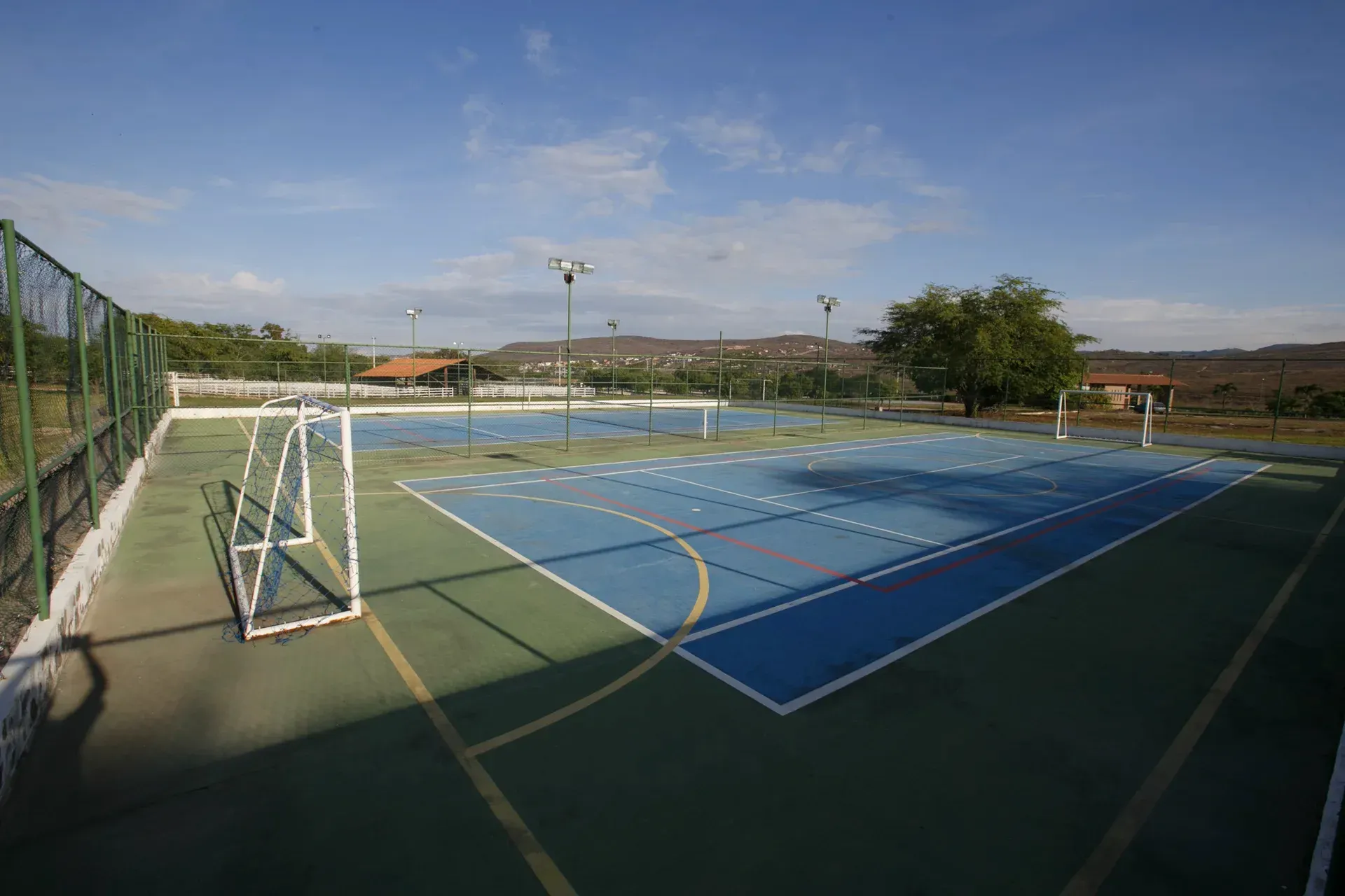 Há uma quadra de tênis e um campo de futebol ao fundo.