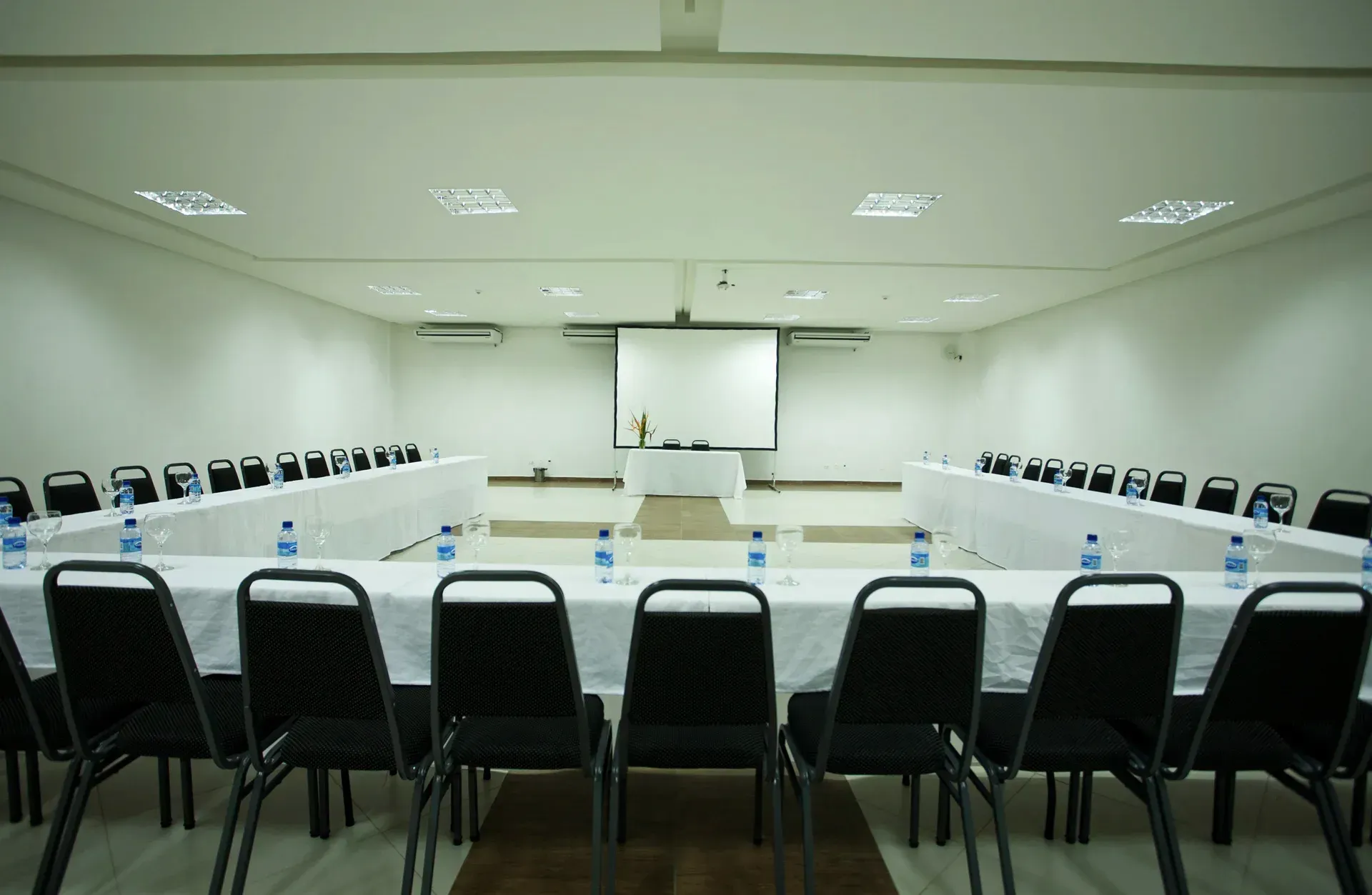Uma sala de conferências com mesas e cadeiras e uma tela de projetor