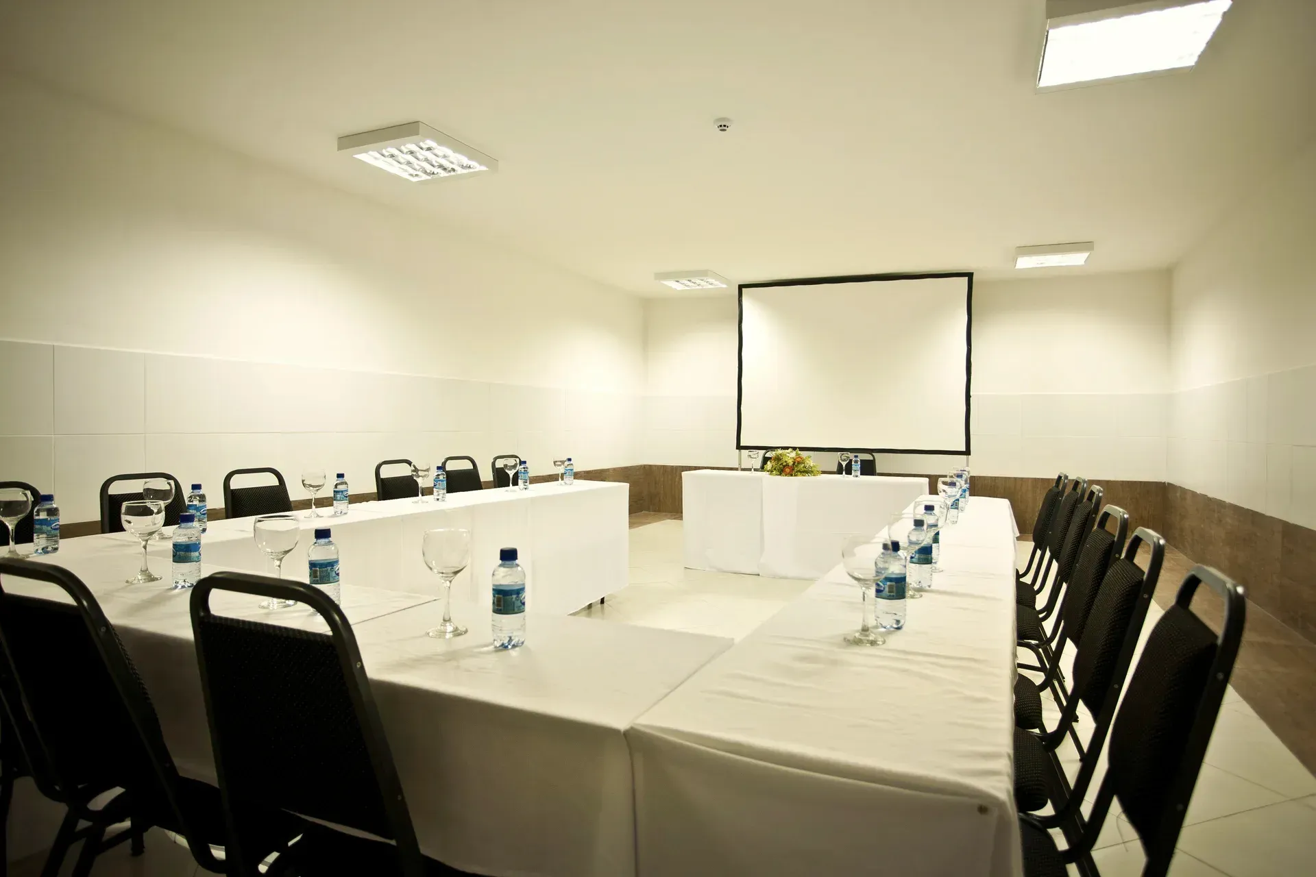 Uma sala de conferências com mesas e cadeiras e uma tela de projetor