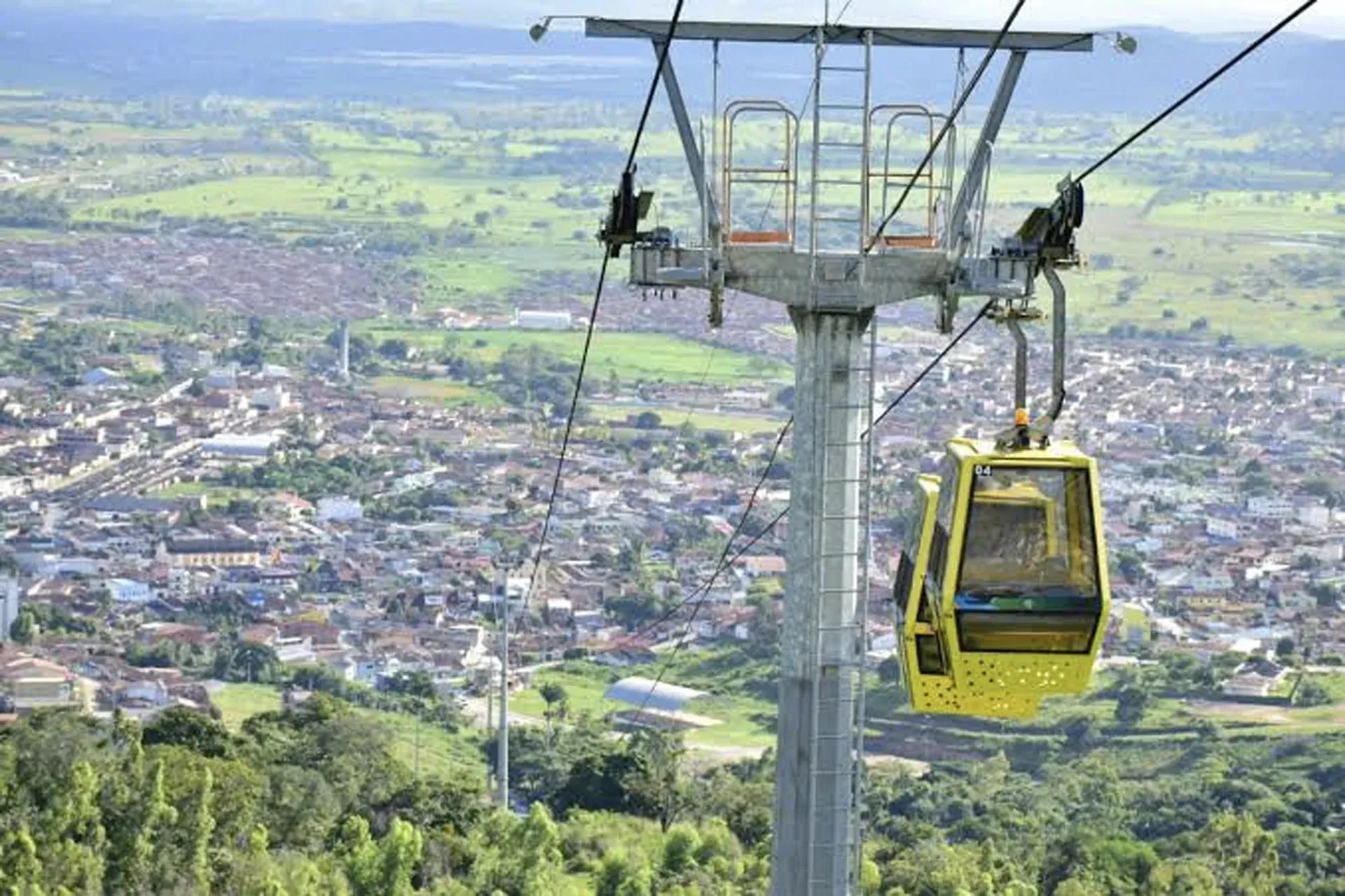 Um teleférico amarelo está subindo uma colina com vista para uma cidade.
