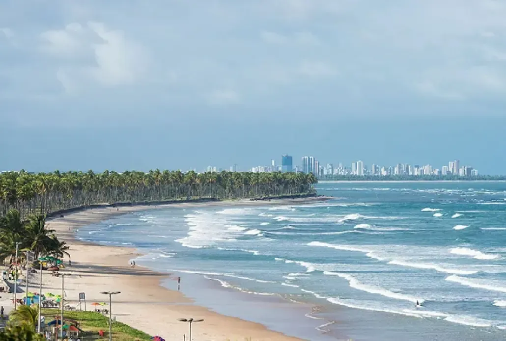 Uma vista aérea de uma praia com palmeiras e uma cidade ao fundo.