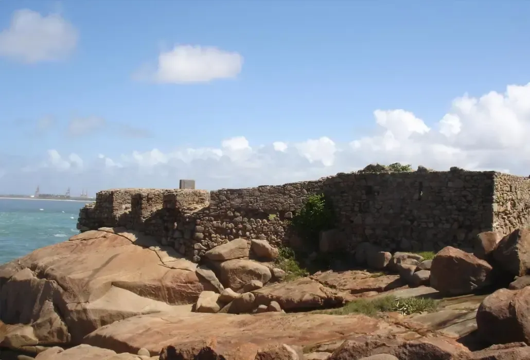 Um penhasco rochoso com vista para o oceano com um muro de pedra em primeiro plano