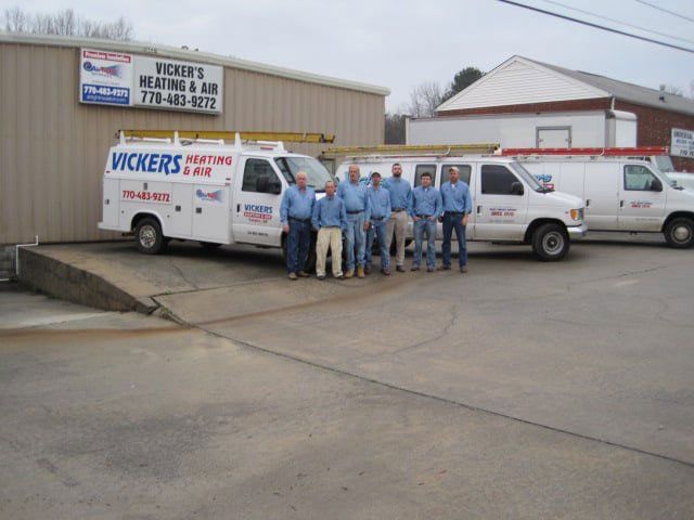 Vickers Heating & Air employees in blue shirts stand with their vans in front of their business.