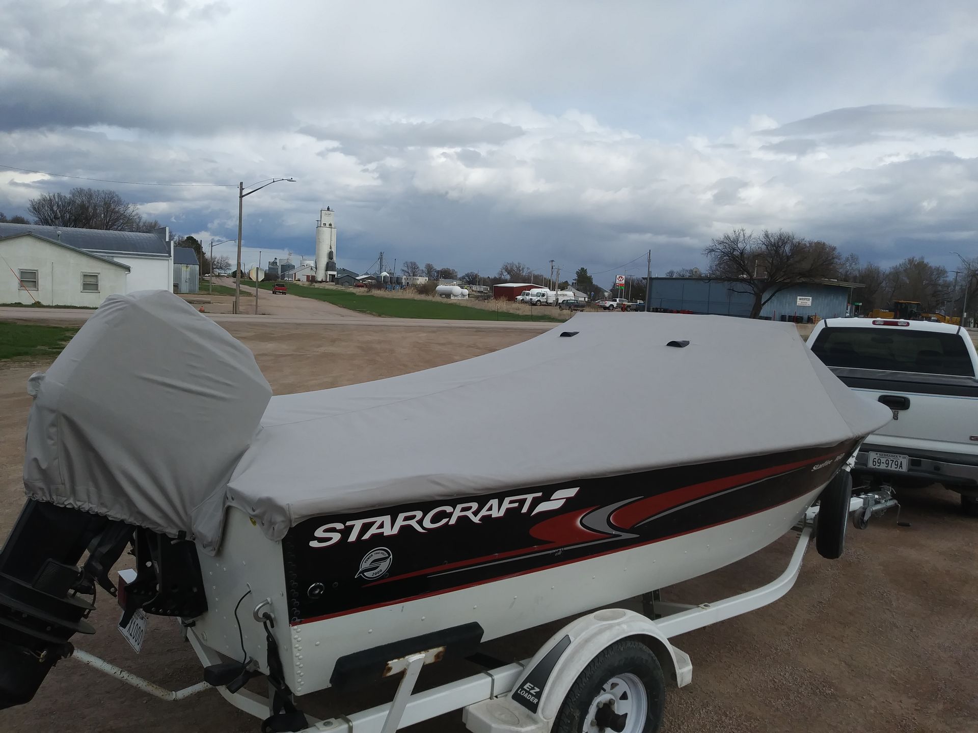 Starcraft boat on a trailer, covered with a gray tarp, parked outdoors under cloudy skies
