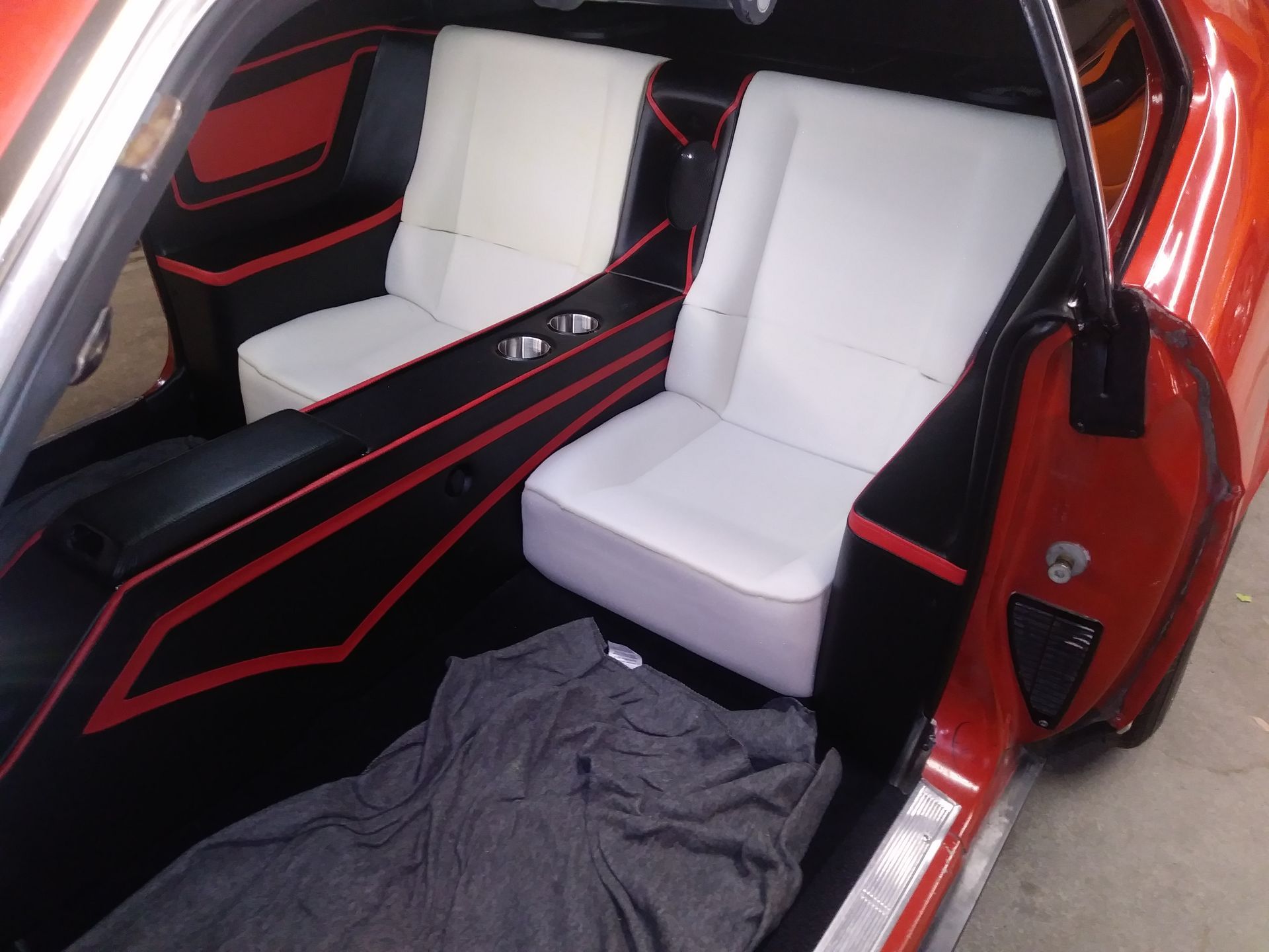 Custom car interior with white bucket seats, black-and-red trim, and an open red door.