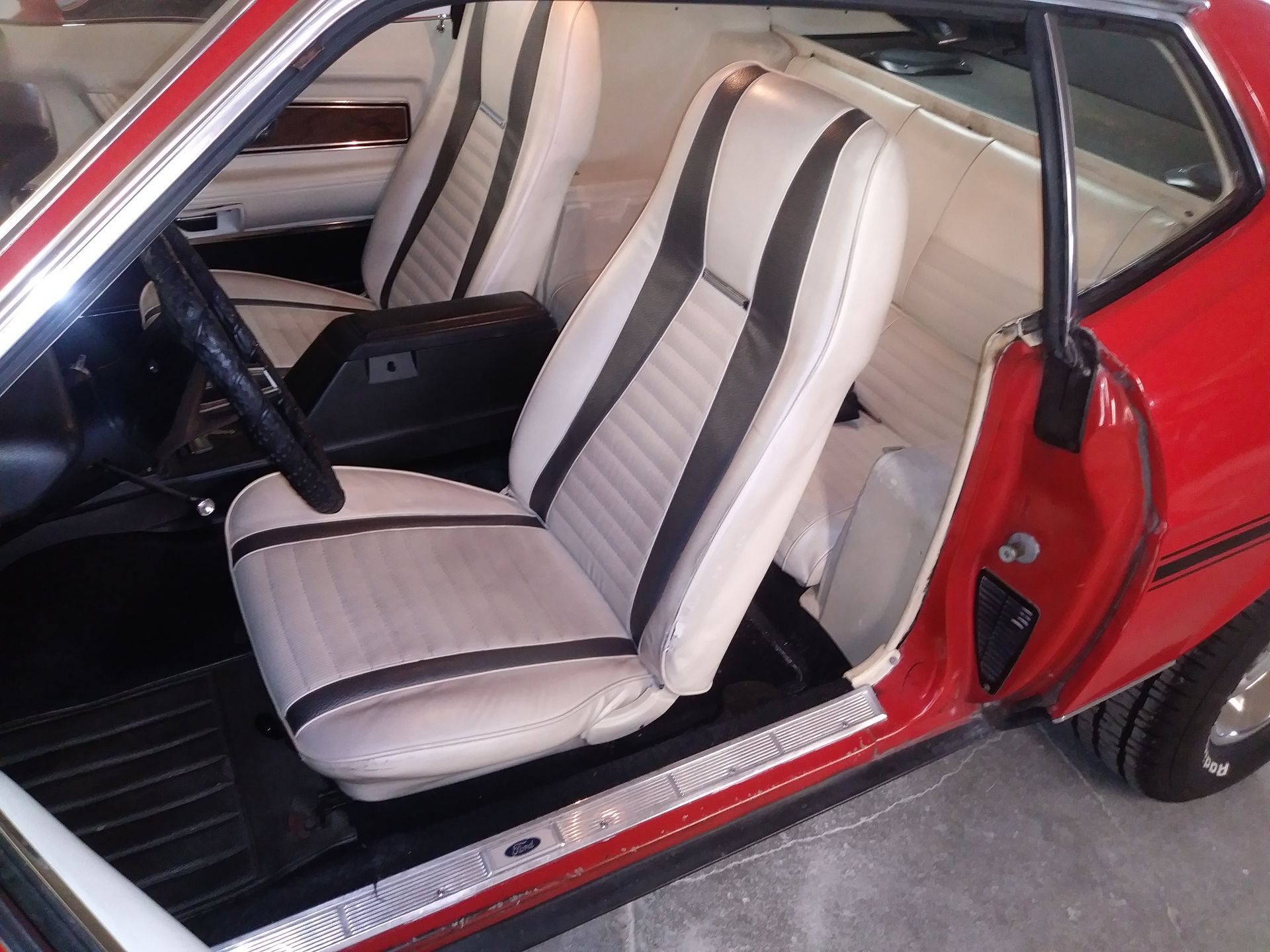 Red classic car interior with white bucket seats and black stripes, viewed through the open door
