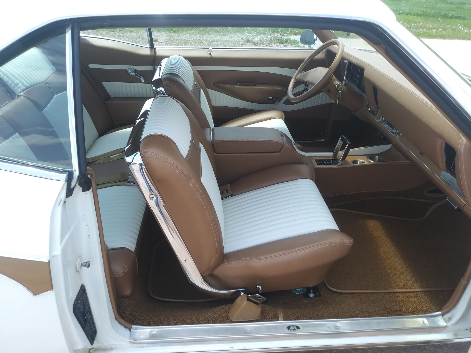 Vintage car interior with brown-and-white seats and tan dashboard, viewed through the open door