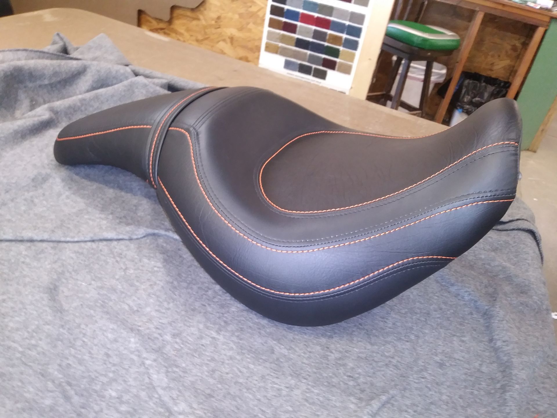 Black motorcycle seat with orange stitching on a gray fabric surface