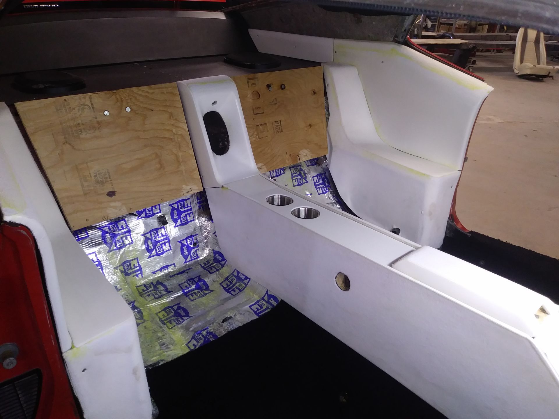 Partially built car interior with white panels, plywood backing, and blue patterned seat covering