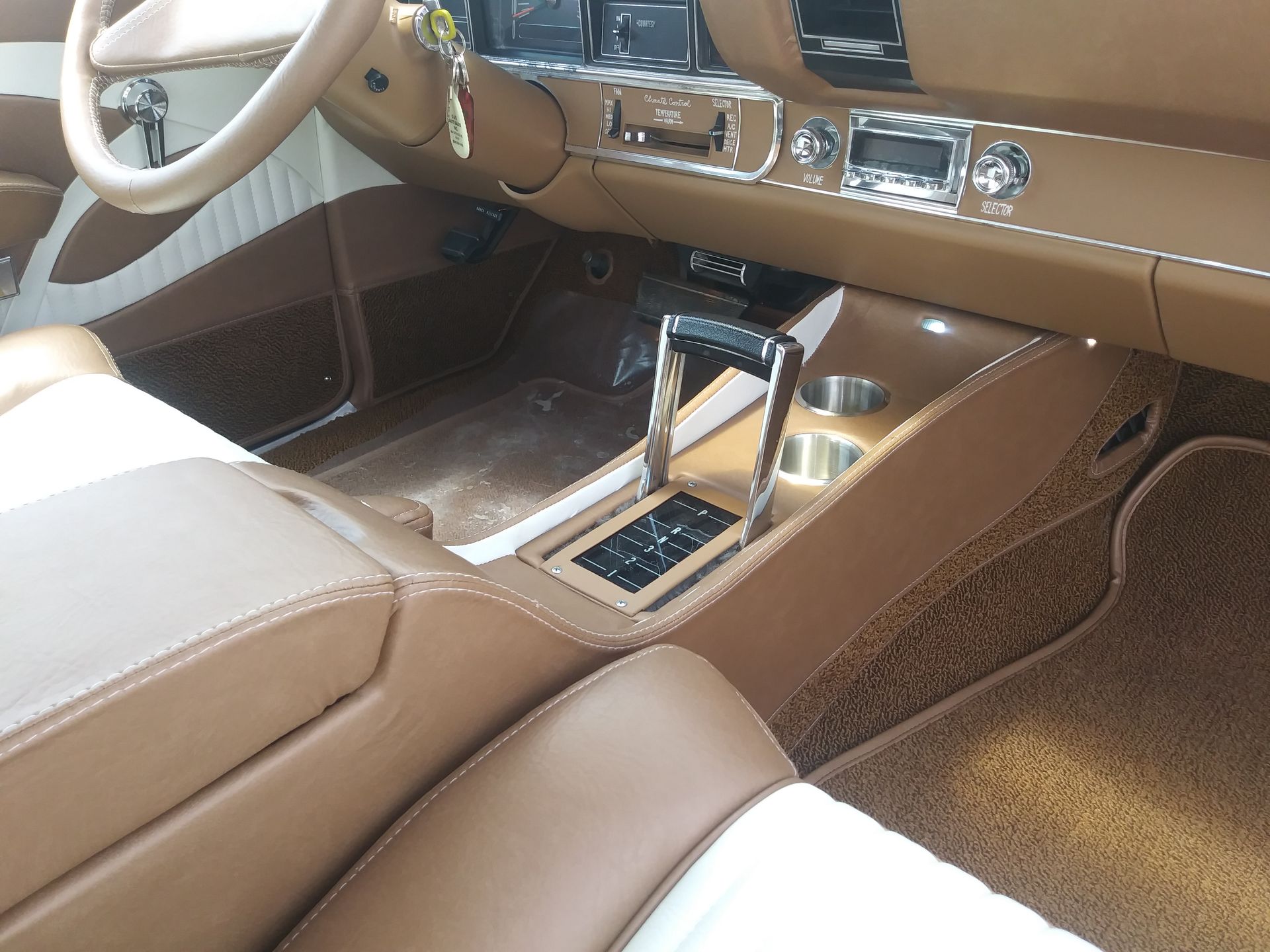 Car interior with tan leather seats and center console, featuring chrome controls and wood trim.