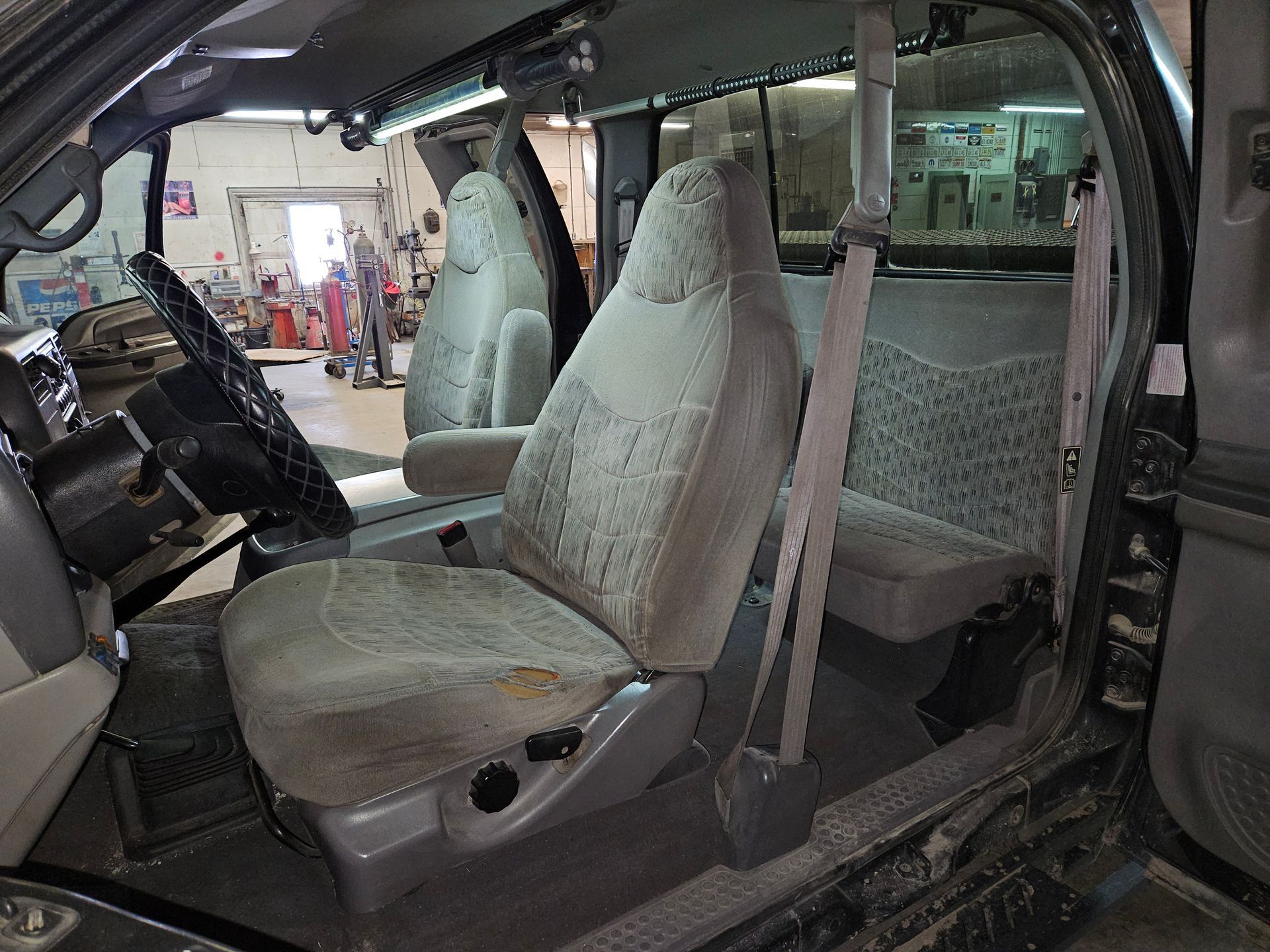 Car interior with light gray seats removed and loose, showing a workshop background