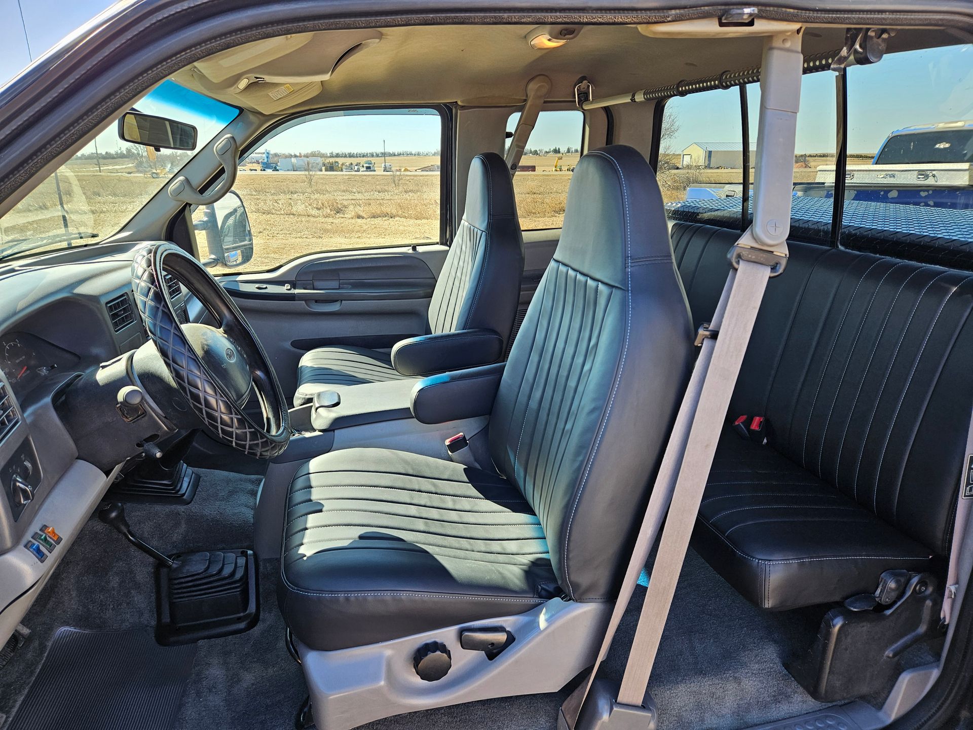 Inside a vehicle cabin with gray seats and steering wheel, viewed from the open passenger side door