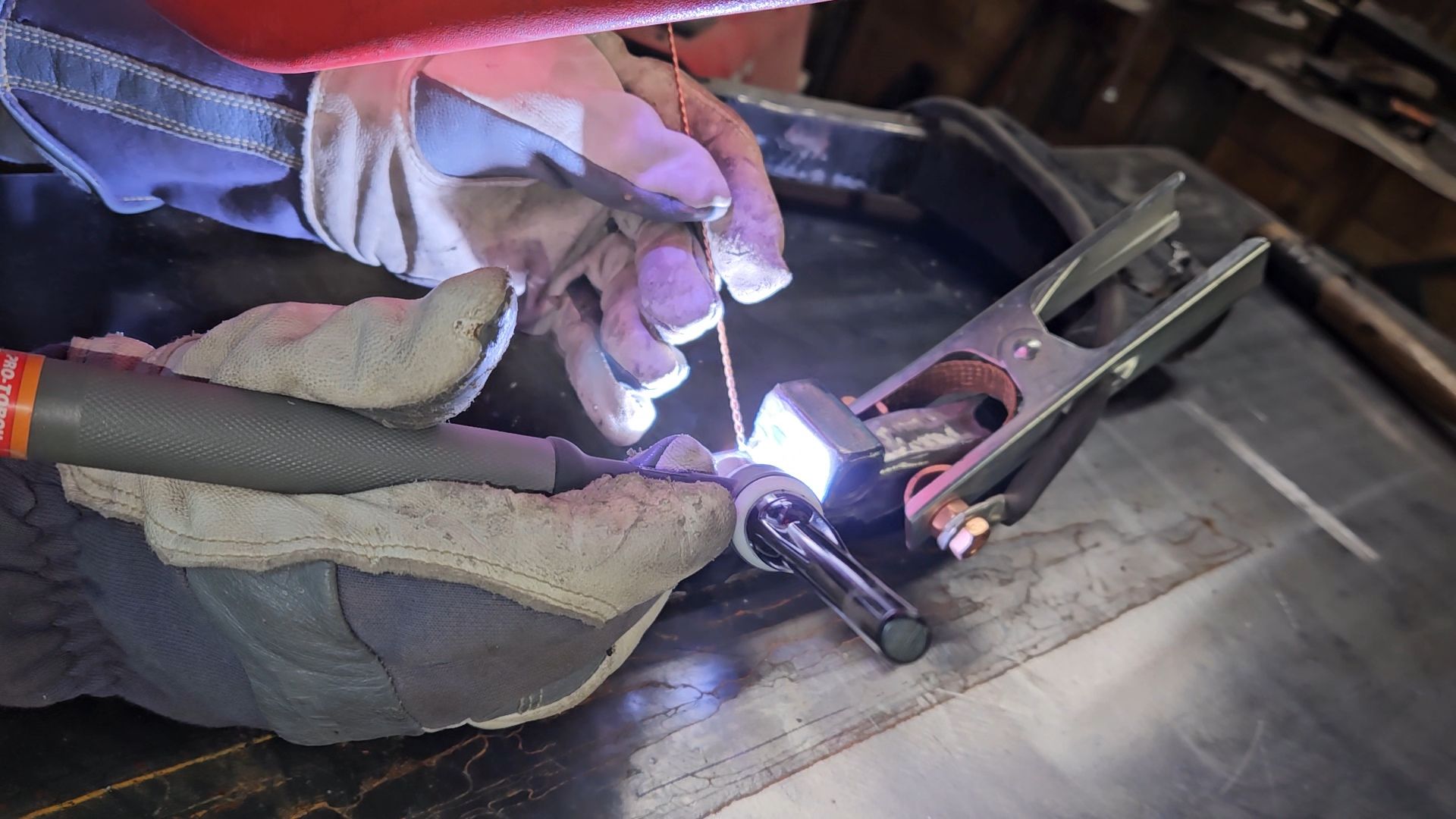 Gloved hands welding a metal bracket with a bright arc light in a workshop