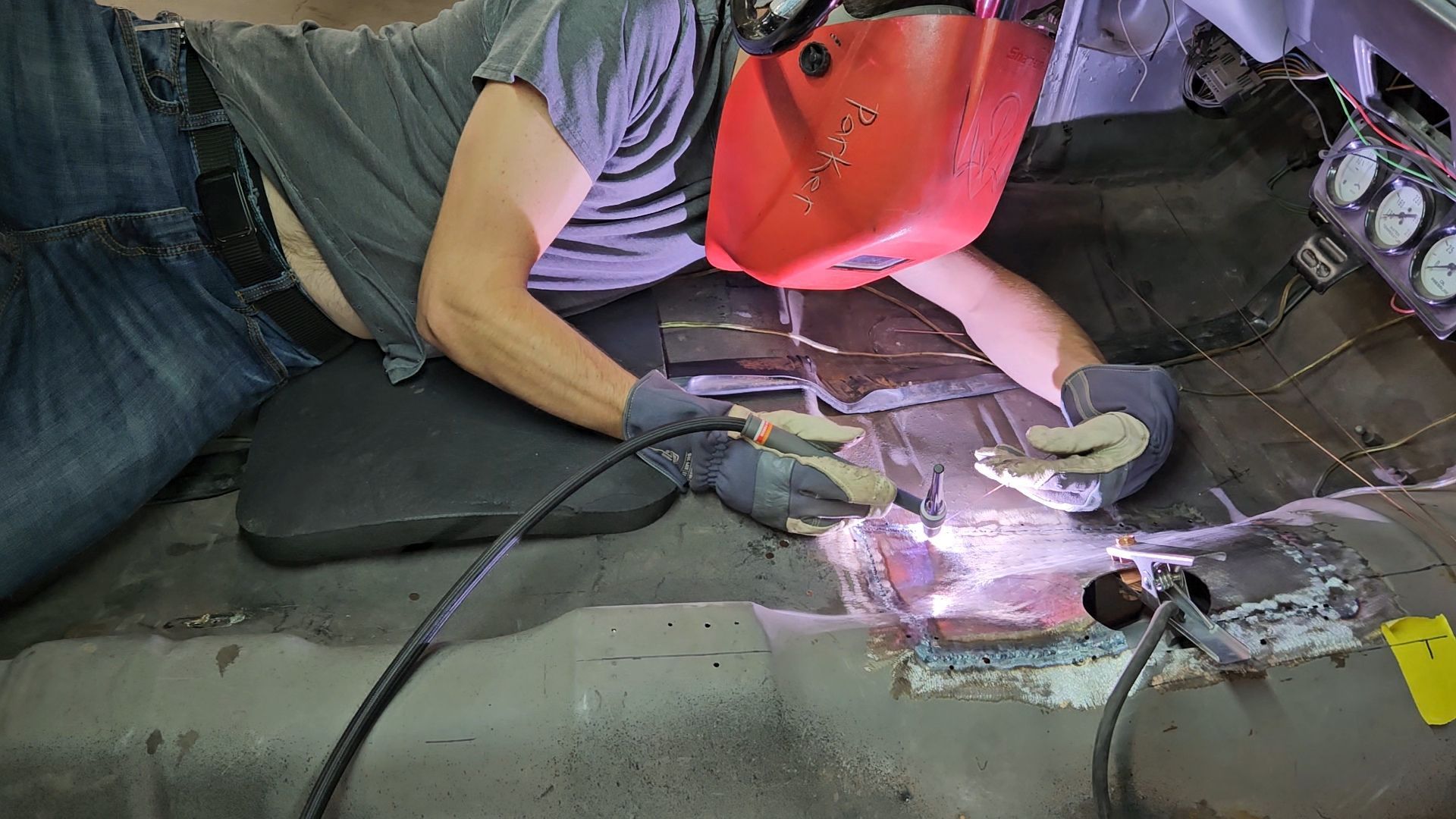 Welders in protective gear repair a metal floor panel, bright arc light illuminating the work area.