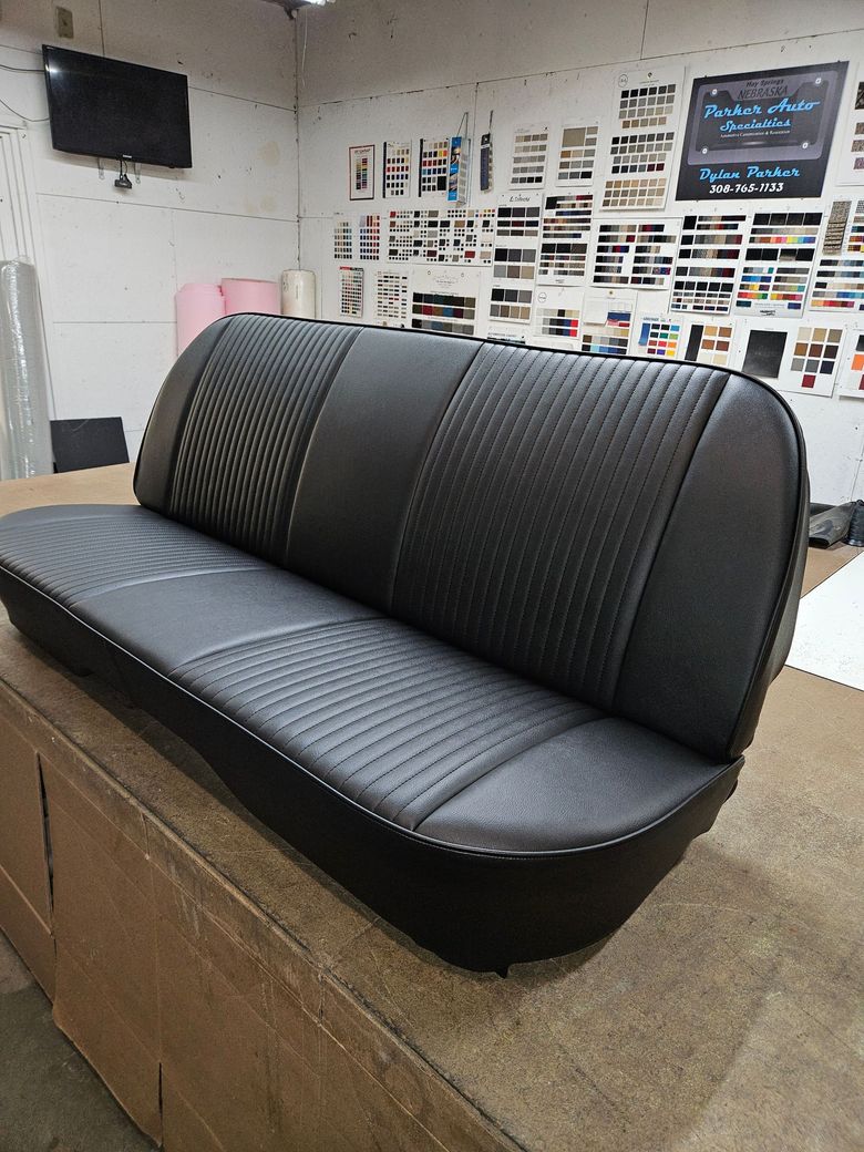 Black vinyl bench seat on a wooden platform in a shop or showroom, with posters on the wall behind.