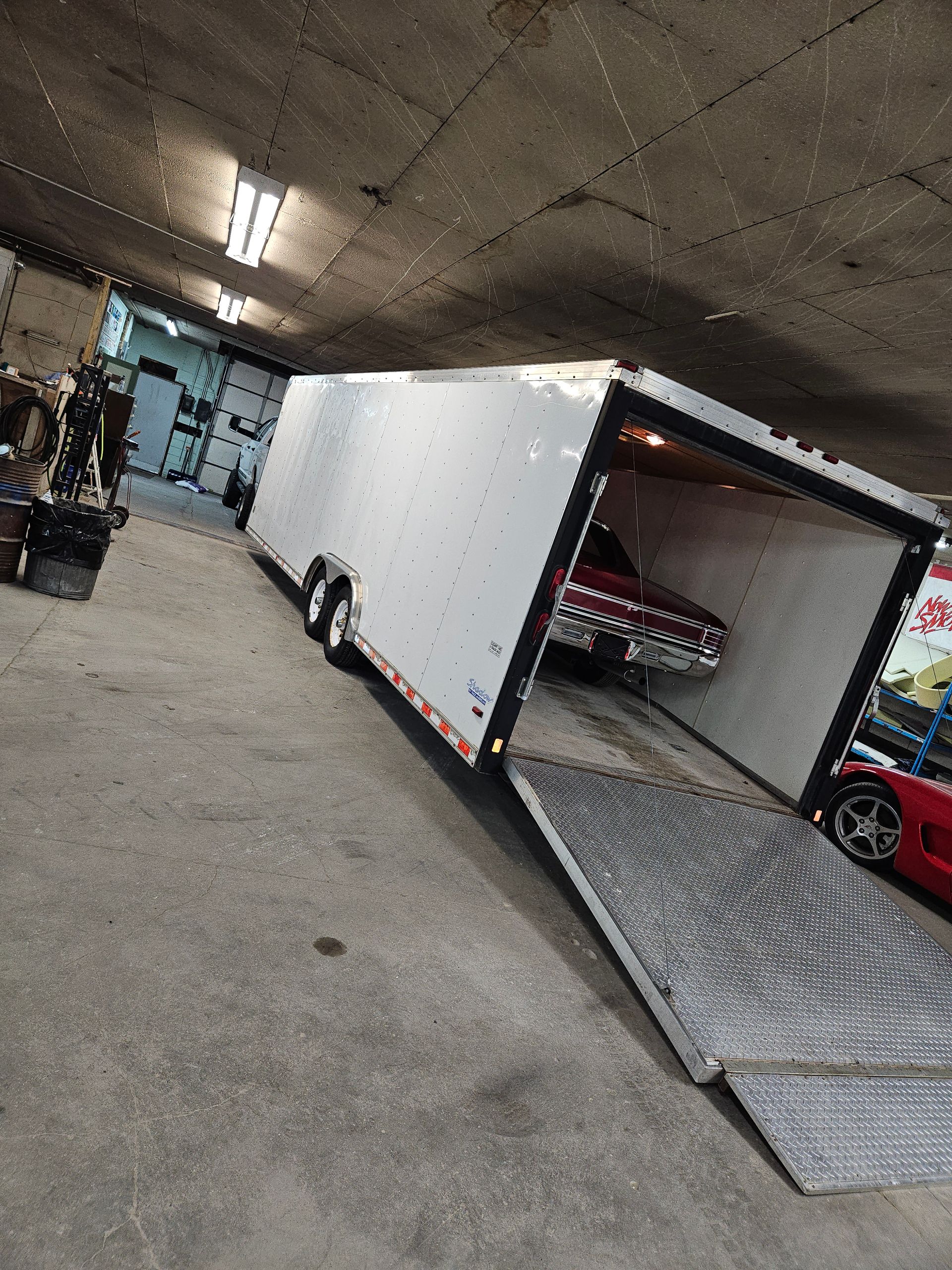 Box truck with open ramp inside a garage, with a red car parked beside it.