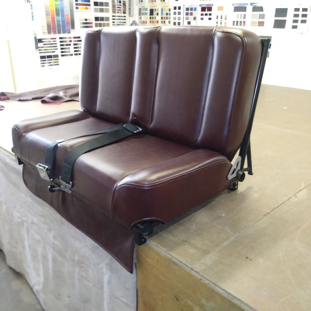 Brown leather bench seat strapped on a platform in a workshop or upholstery studio.