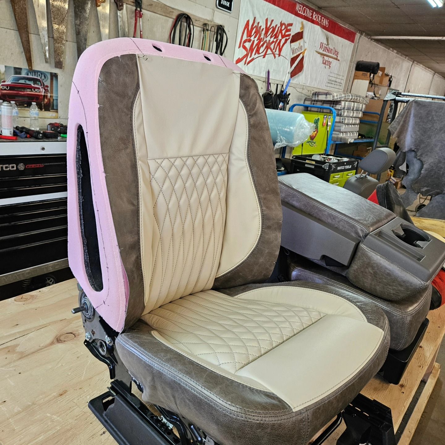 Pink-and-cream upholstered car seat in a workshop, with tools and parts in the background