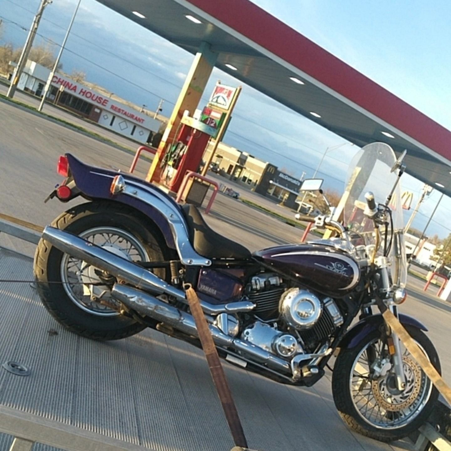 Black cruiser motorcycle parked at a gas station under a red canopy