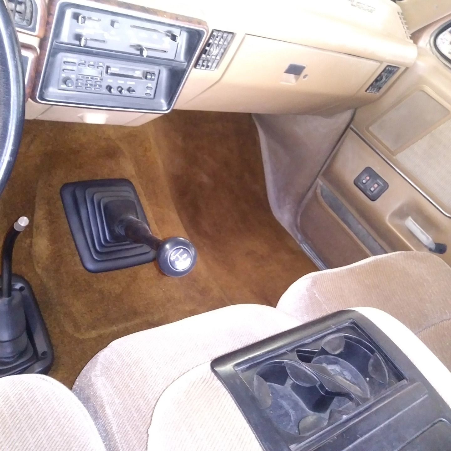 Tan car interior with manual gear shift, cassette stereo, and beige seats