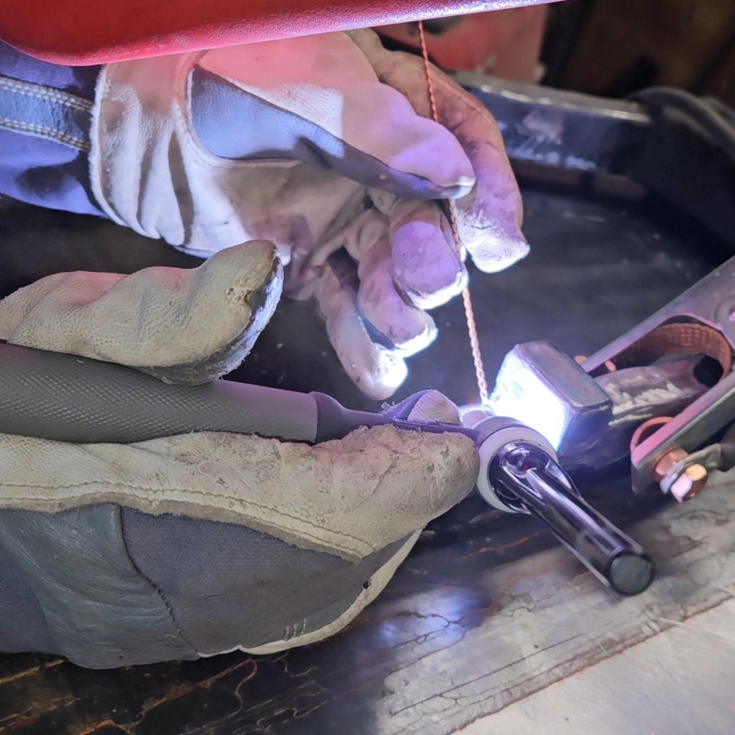 Gloved hands welding a metal rod with bright sparks in a workshop