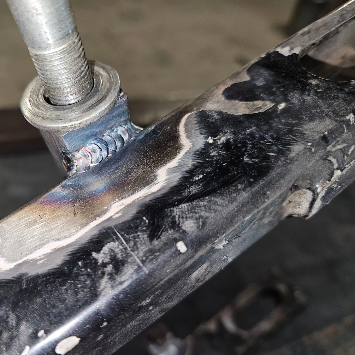 Close-up of a welded metal joint with blue heat discoloration on a dark surface.