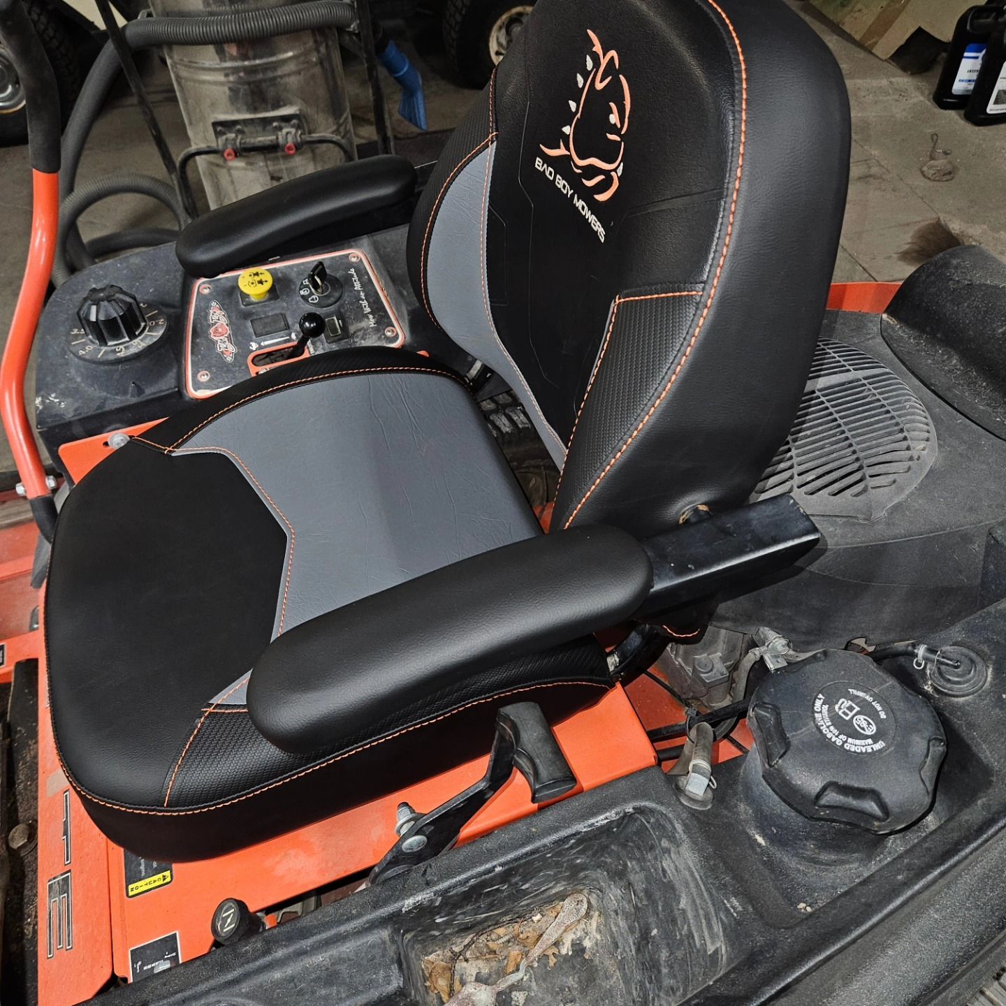 Black and gray mower seat with armrest on orange lawn equipment inside a garage