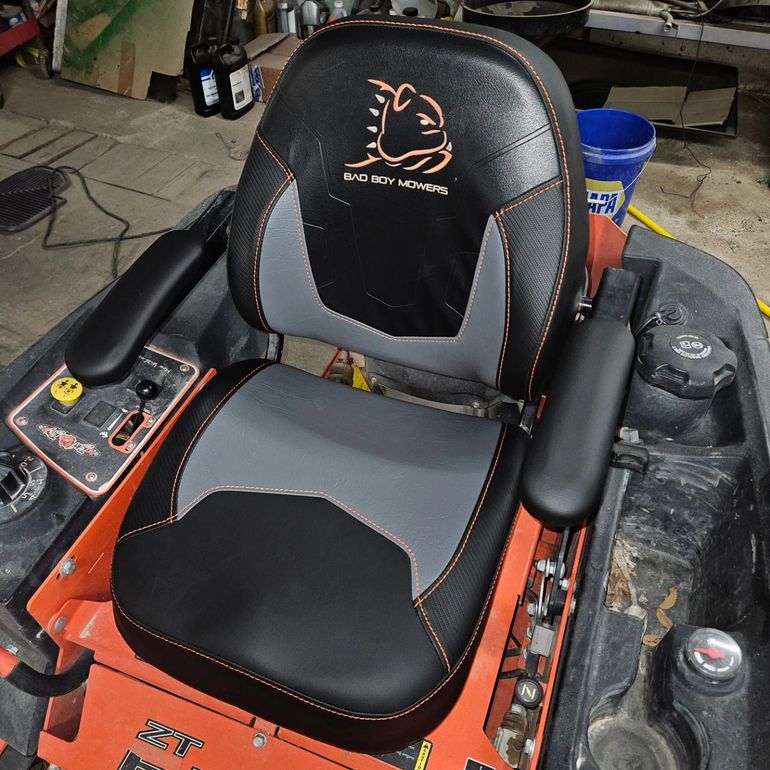 Orange-and-black riding lawn mower seat with armrests and control panel in a garage