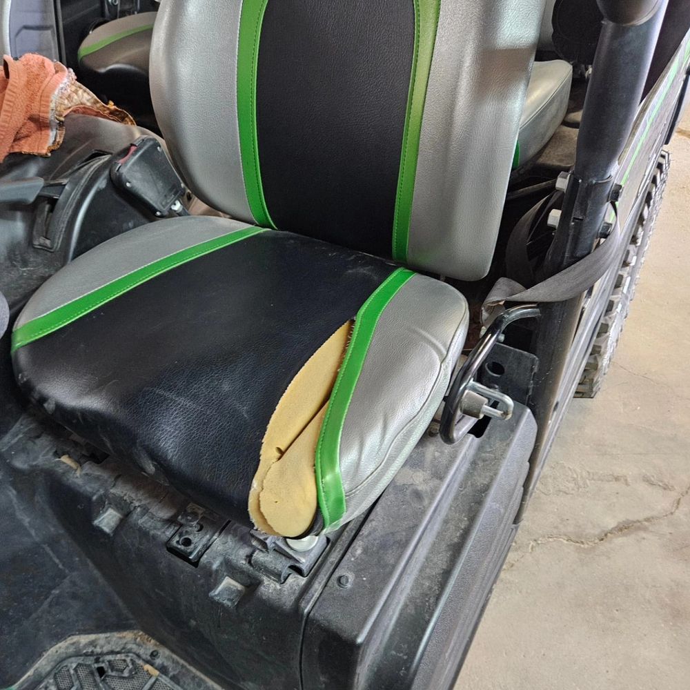 Damaged black and green car seat with torn cushion and exposed yellow foam