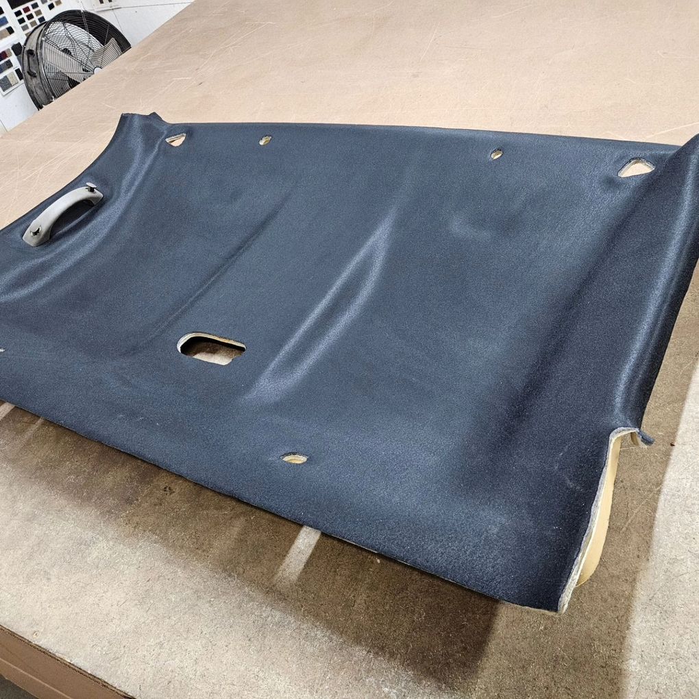 Blue fabric seat or cushion cover lying on a beige surface, with cutout holes and white trim along the edges
