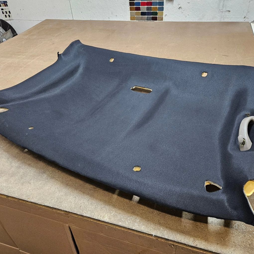 Dark gray molded car headliner panel on a worktable with cutouts and handles visible