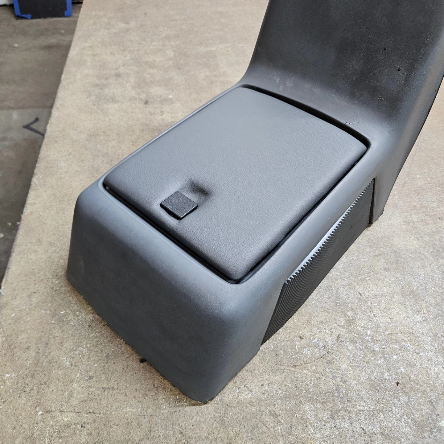Black molded plastic seat base with a small latch on top, shown on a concrete floor.