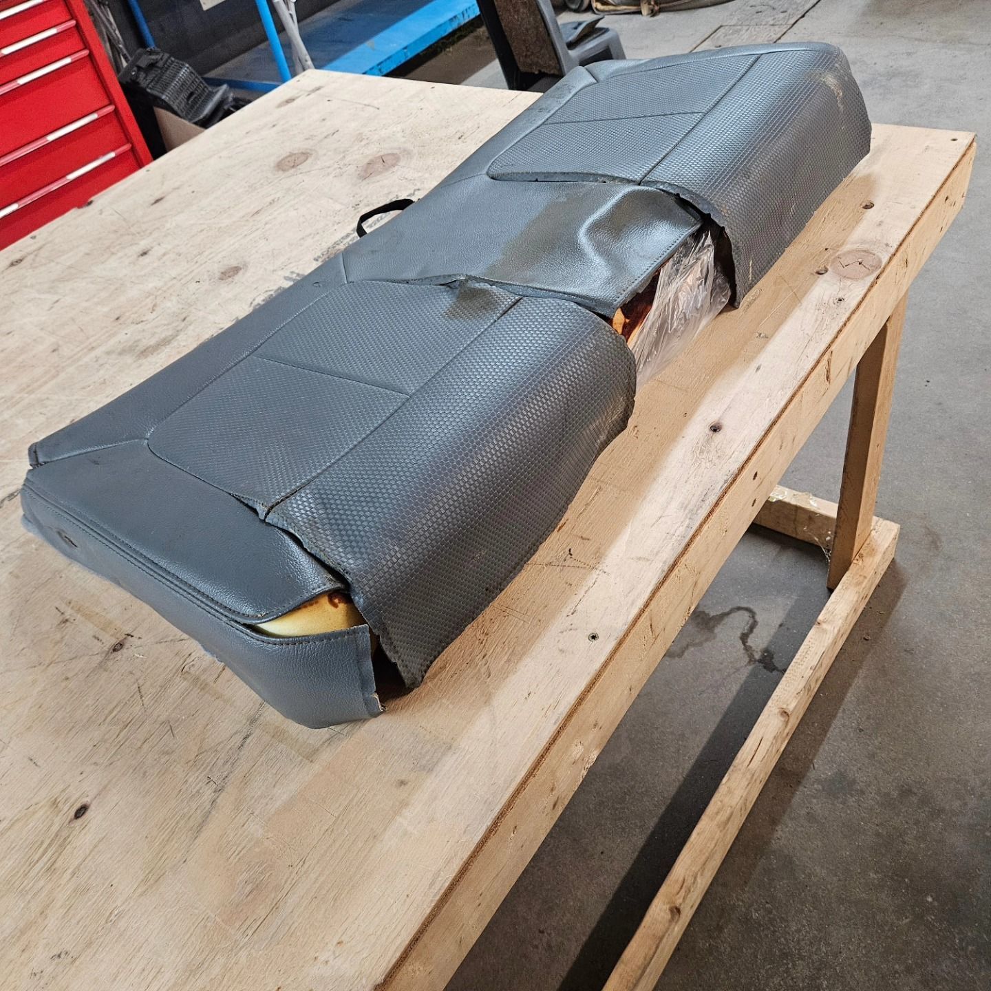 Torn gray vinyl seat cushion on a wooden workbench in a workshop