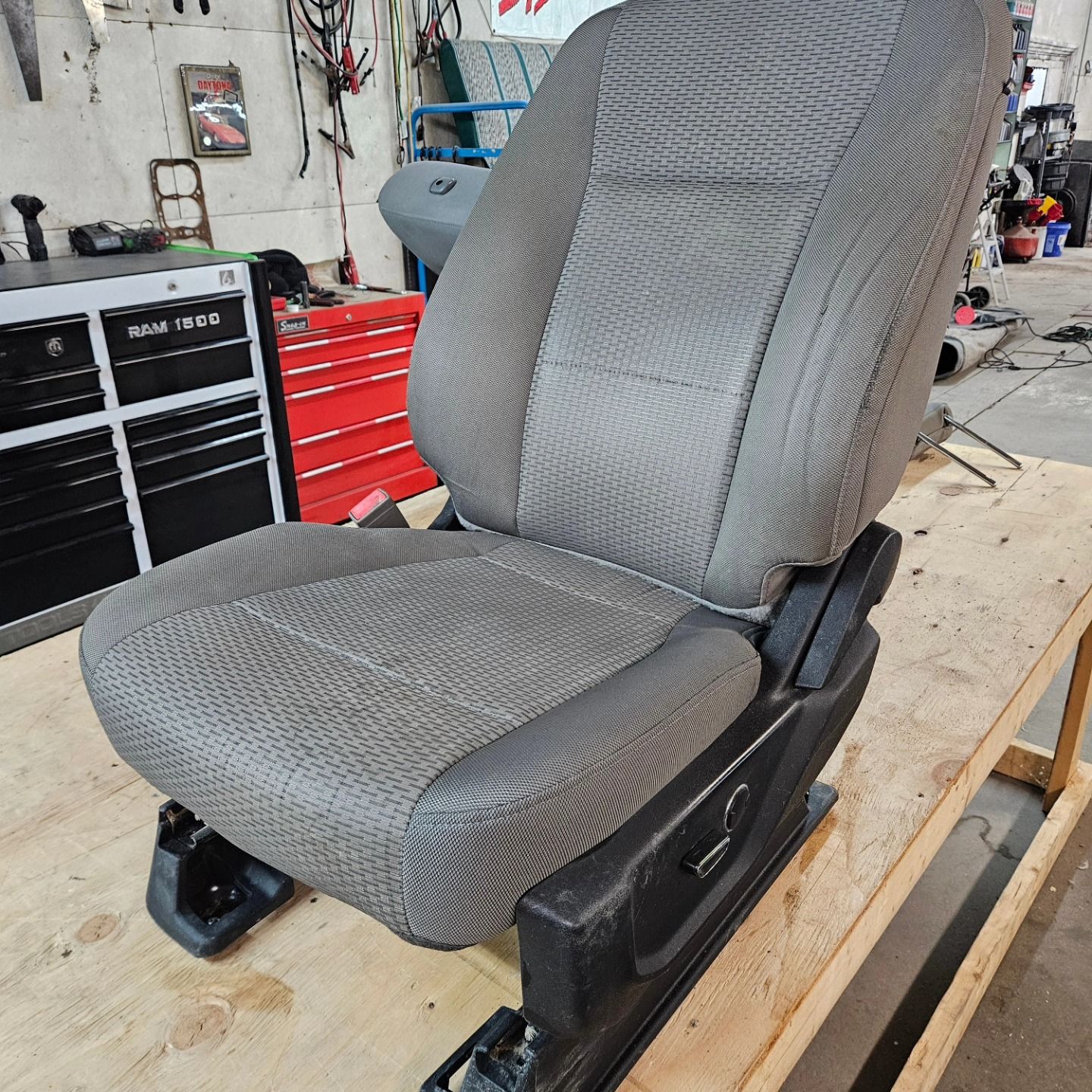 Gray car seat on a wooden workbench in an auto repair shop.