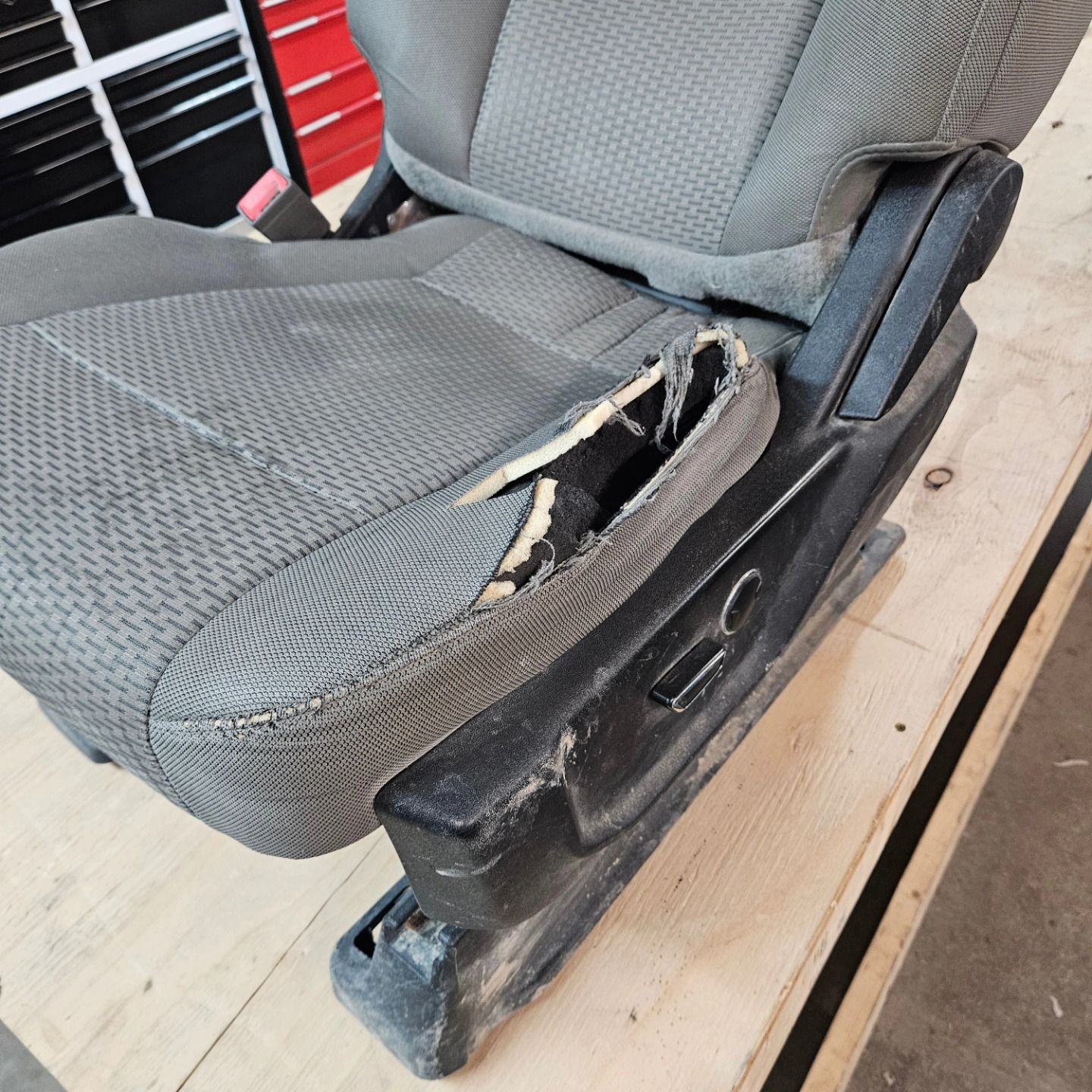 Torn gray car seat upholstery with exposed foam and damaged black seat base inside a vehicle
