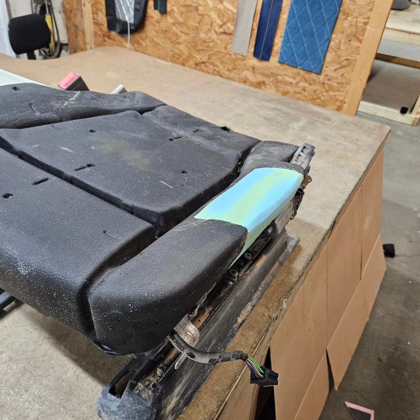 Folded black seat cushion with a blue-green panel on a workshop table