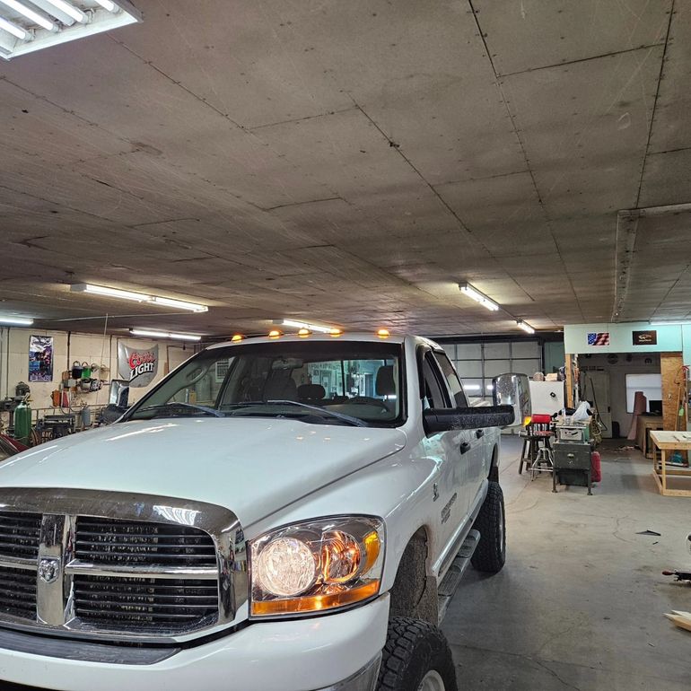 White pickup truck parked inside a garage with fluorescent lights and tools in the background